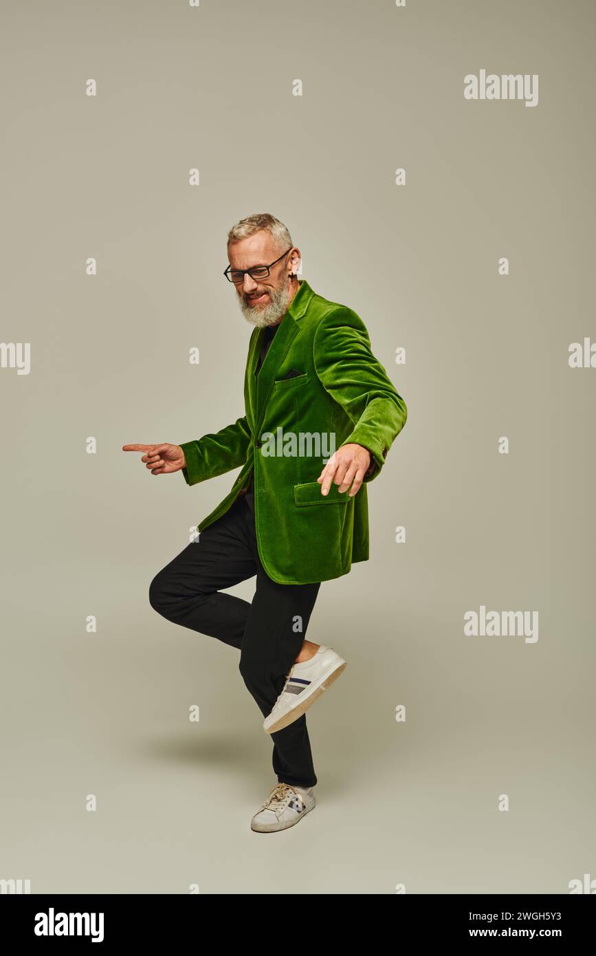 Gut aussehendes, reifes Männermodell in grünem Blazer, das auf einem Bein steht und glücklich lächelt Stockfoto