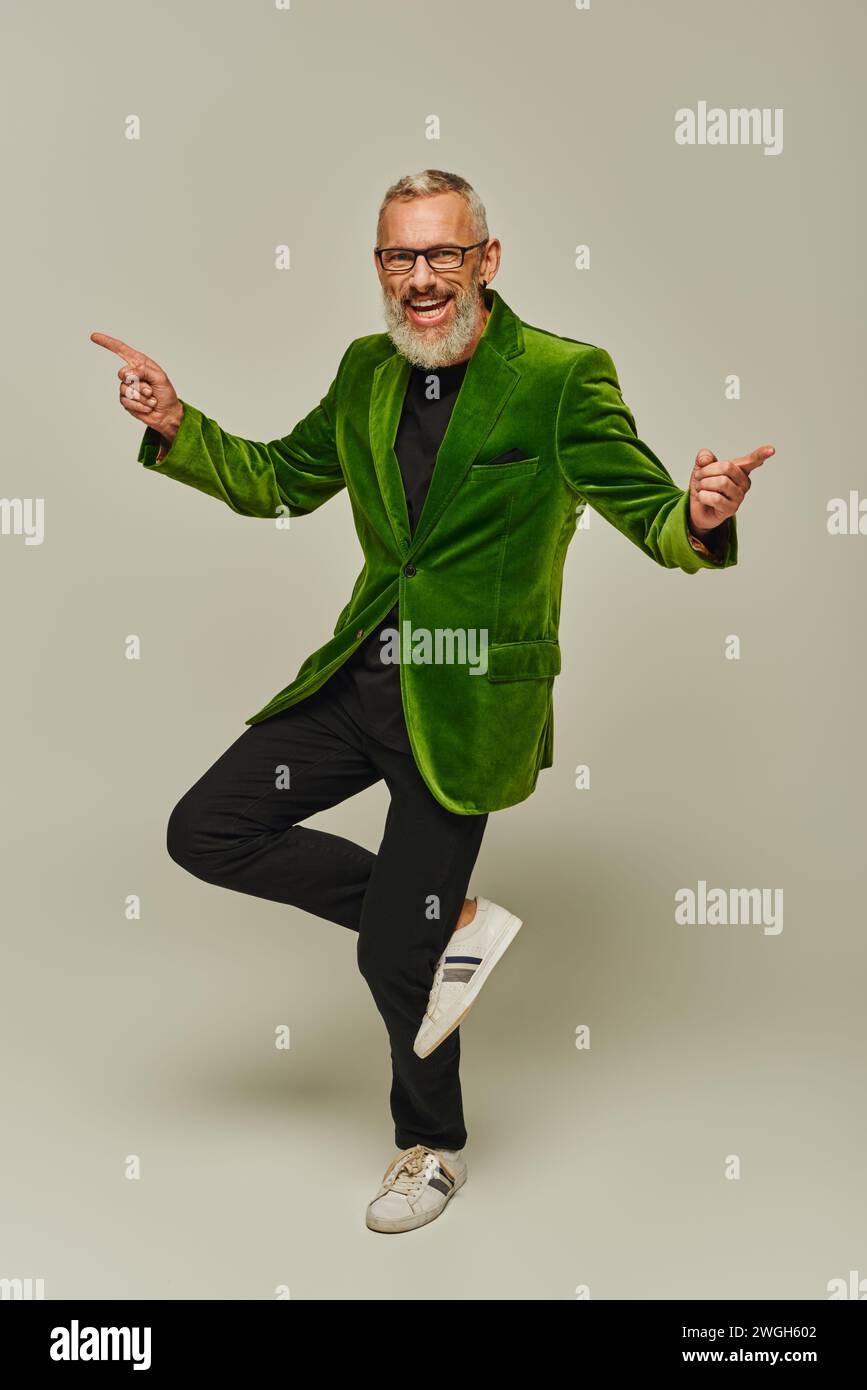 Gutaussehender, fröhlicher reifer Mann in leuchtend grünem Blazer, der auf einem Bein posiert und in die Kamera lächelt Stockfoto