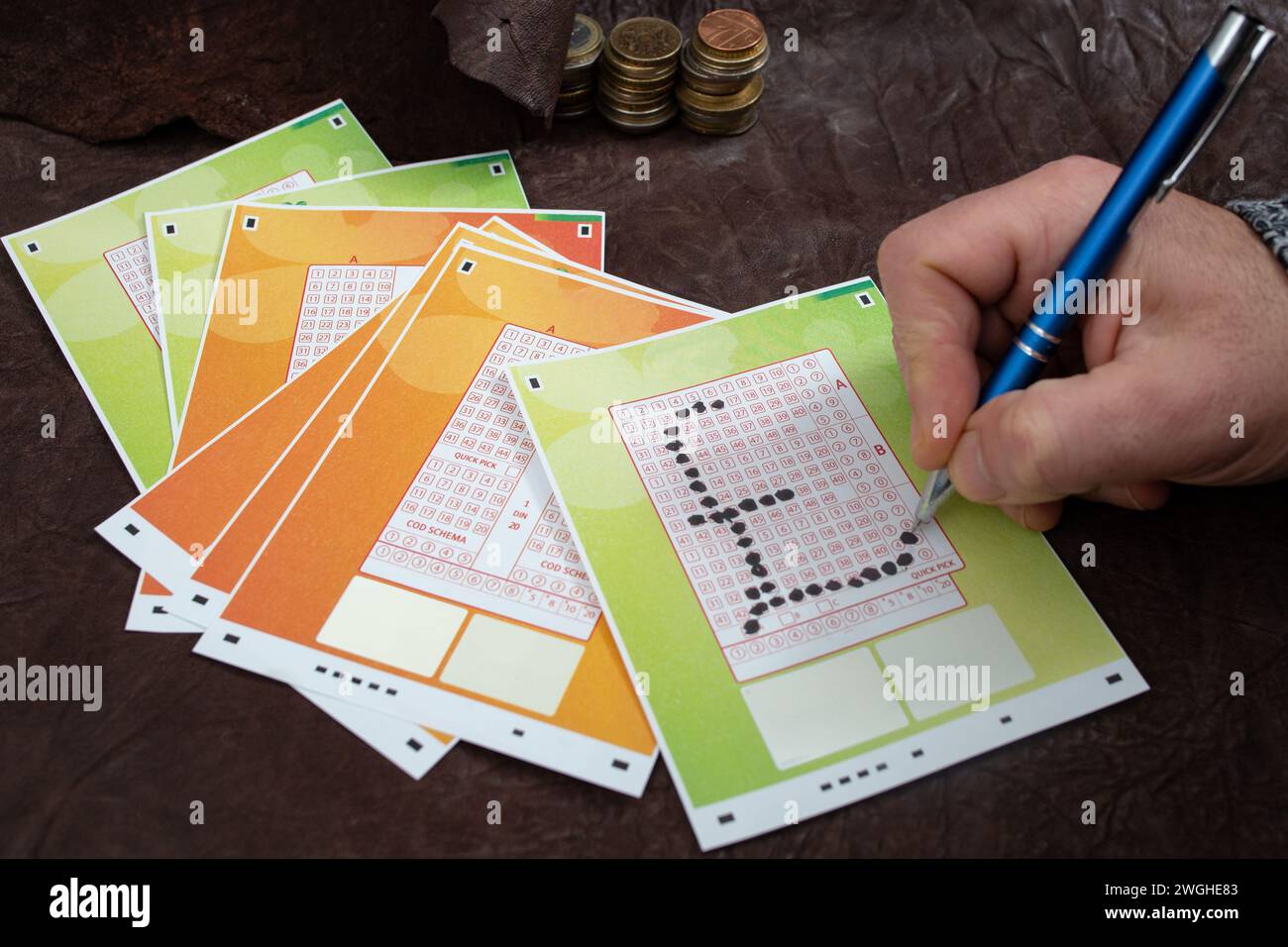 Männliche Hand, die Zahlen auf einem Lotterieschein in Form eines britischen Pfund-Währungssymbols auf einem Schreibtisch aus echtem Leder wählt Stockfoto