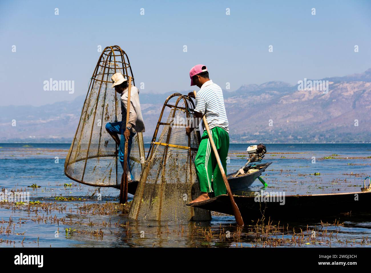 Zwei Personen auf einem kleinen Boot, das Netze im Wasser in der Nähe eines majestätischen Berges benutzt Stockfoto