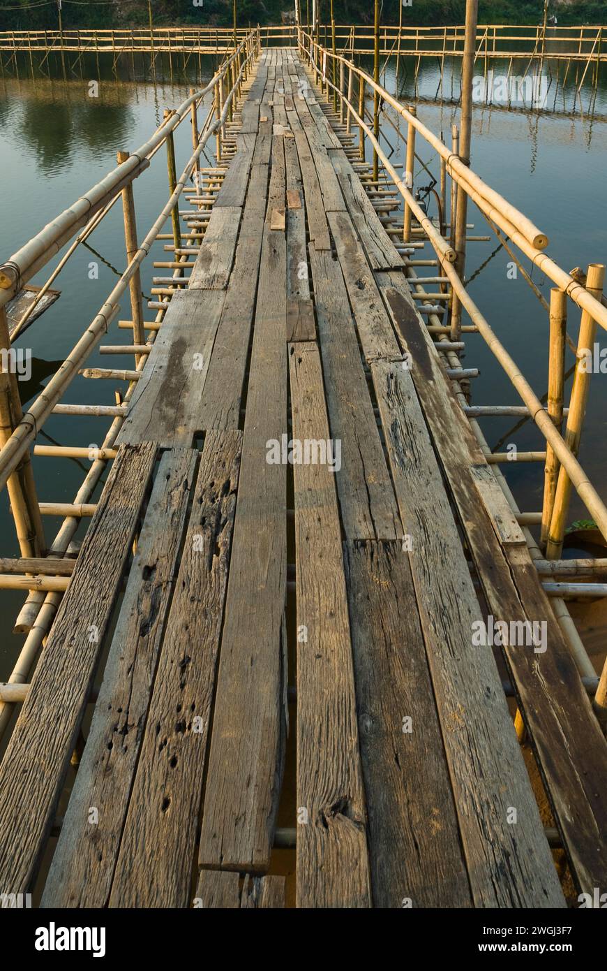 Holzsteg über Wasser mit Dock, eingerahmt von majestätischen Bergen und üppigen Bäumen Stockfoto
