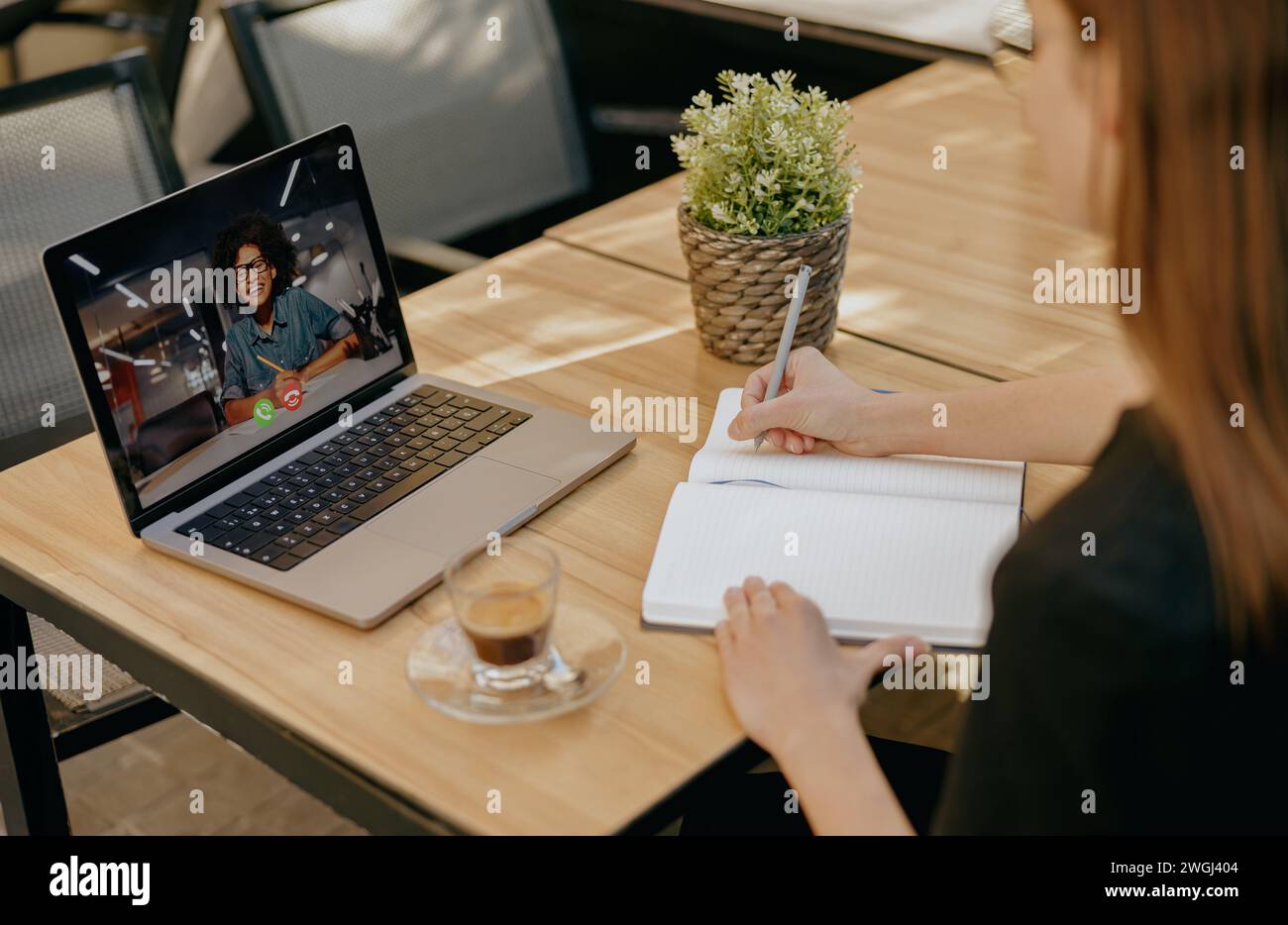 Geschäftsfrau, die mit dem Kunden per Videoanruf spricht und Notizen macht, während sie auf der Terrasse des Cafés sitzt Stockfoto