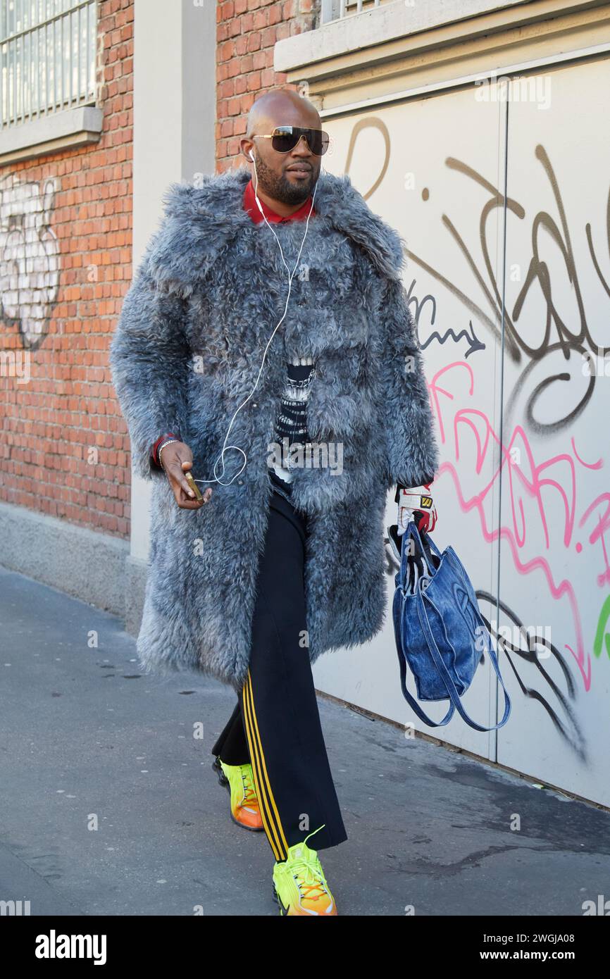 MAILAND, ITALIEN - 13. JANUAR 2024: Mann mit grauem Pelzmantel und gelben fluoreszierenden Sneakers vor der Fendi Fashion Show, Mailand Fashion Week Street Style Stockfoto
