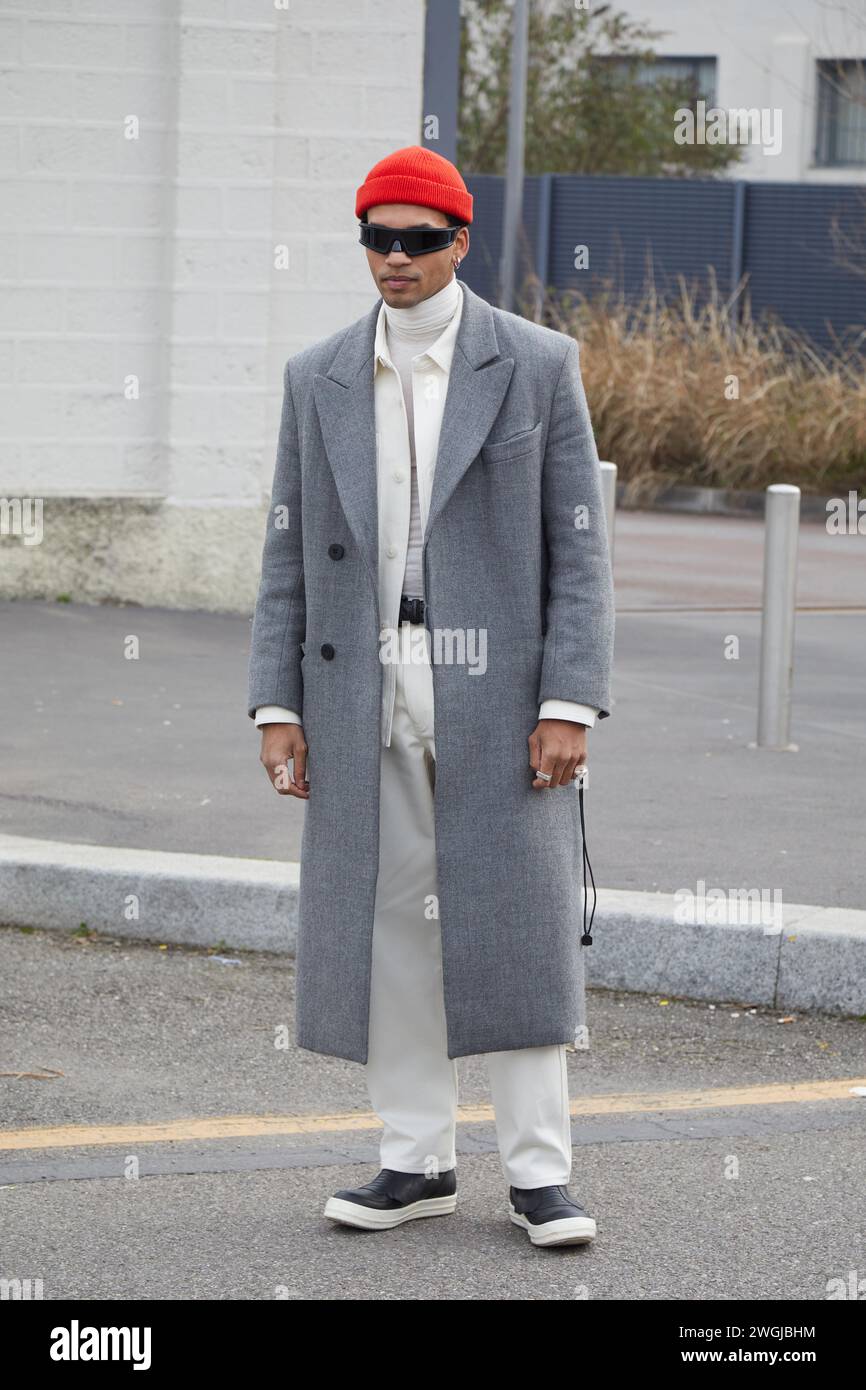 MAILAND, ITALIEN - 14. JANUAR 2024: Mann mit grauem Mantel, weißer Hose und roter Wollmütze vor der Prada Fashion Show, Mailand Fashion Week Street Style Stockfoto