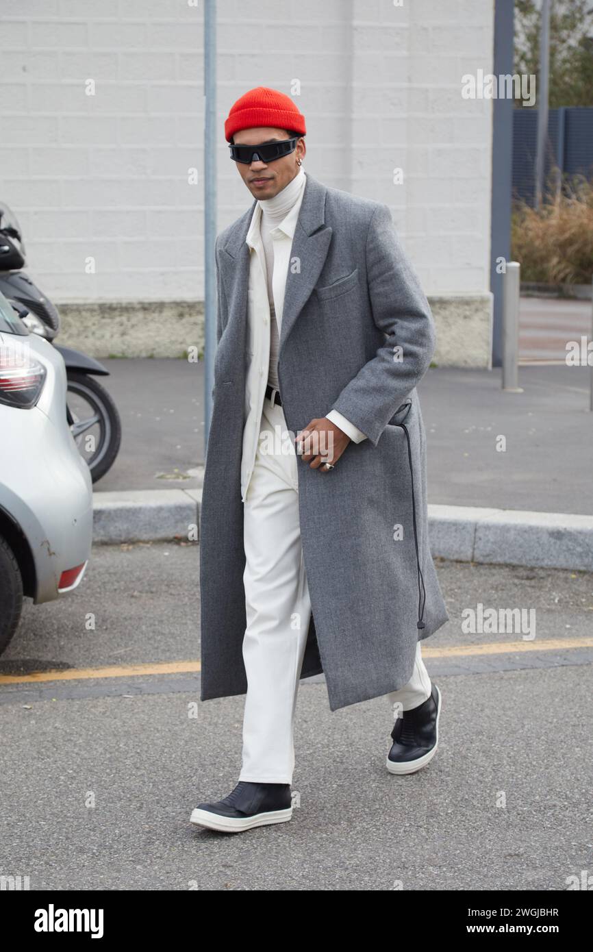 MAILAND, ITALIEN - 14. JANUAR 2024: Mann mit grauem Mantel, weißer Hose und roter Wollmütze vor der Prada Fashion Show, Mailand Fashion Week Street Style Stockfoto