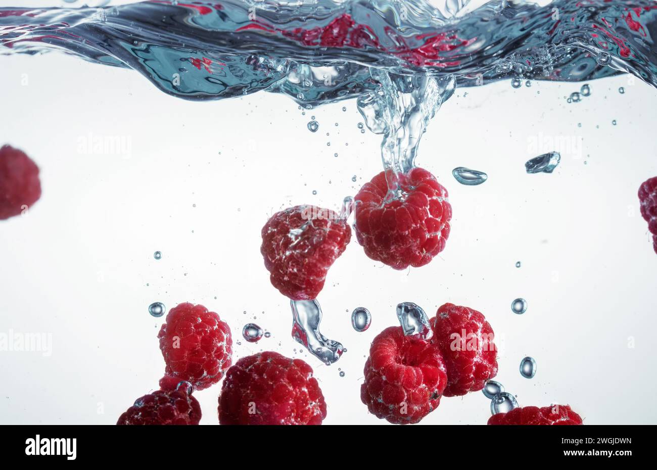 Himbeeren fallen mit Spritzern und Luftblasen ins Wasser. Selektiver Fokus. Stockfoto