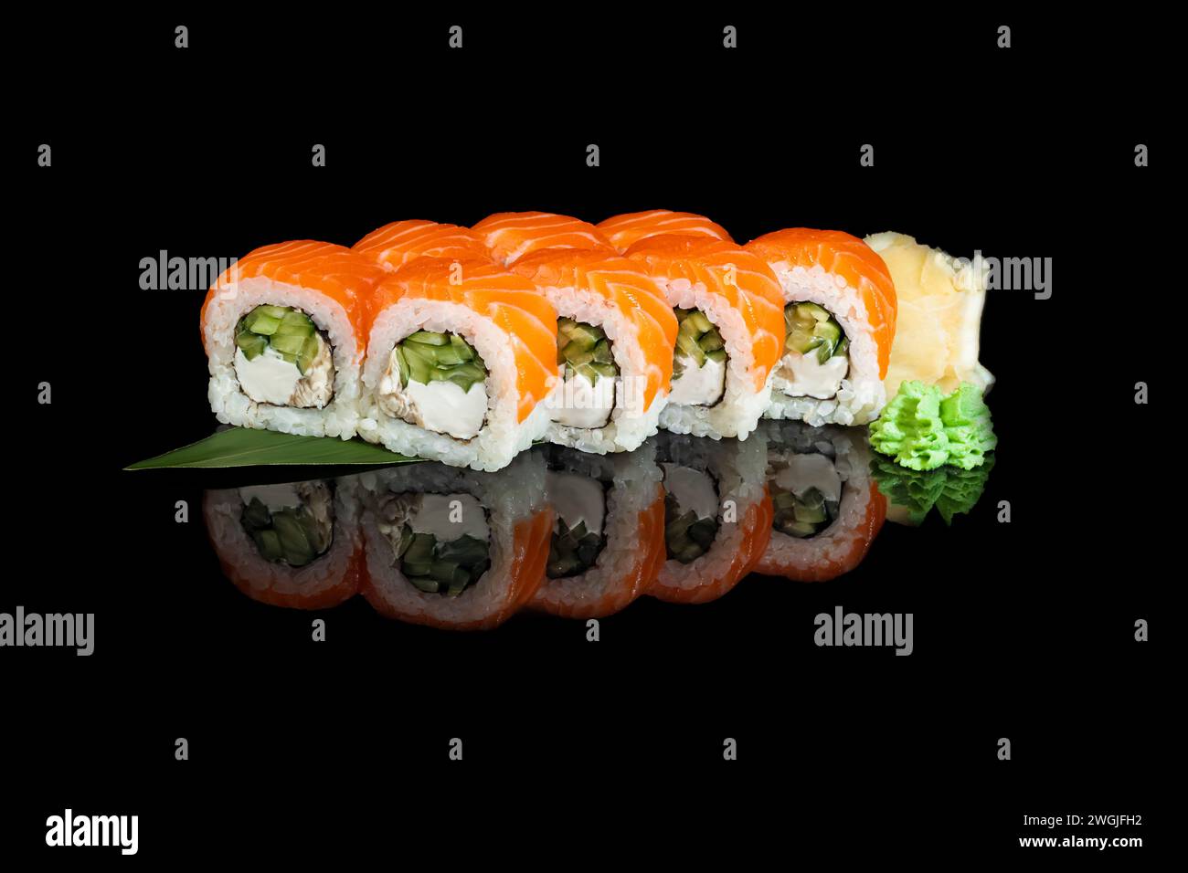 Sushi-Sets Uramaki, Kalifornien, Philadelphia, auf einem weißen Teller. Festliches Neujahrskonzept. Vor einem dunklen reflektierenden Hintergrund. Stockfoto