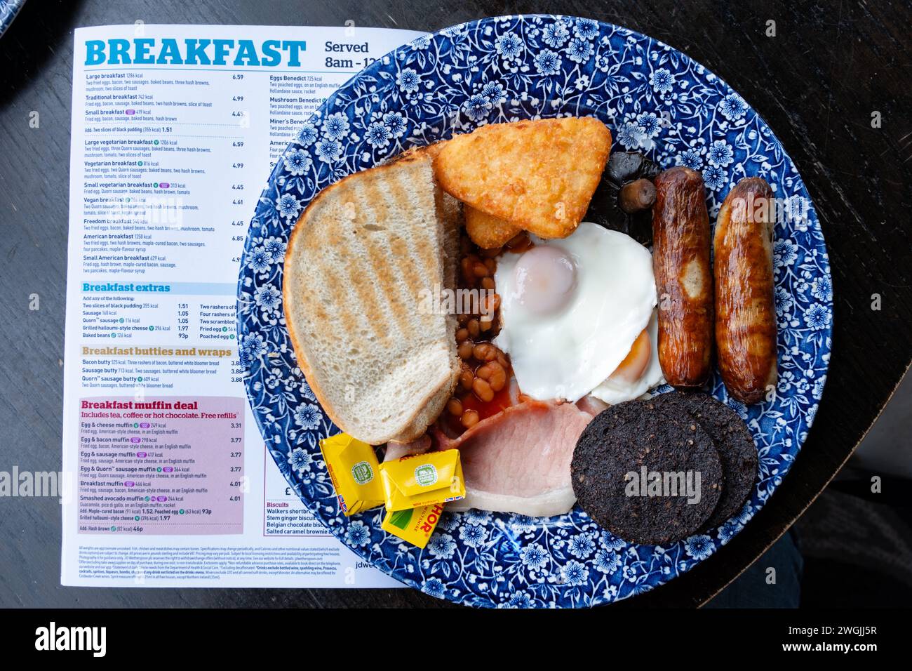 Ein großes Wetherspoons-Frühstück, das in einem Wetherspoons-Pub serviert wird. Das Frühstück kostet 1286 Kalorien. Die Karte des Pub-Frühstücks befindet sich neben dem Teller Stockfoto