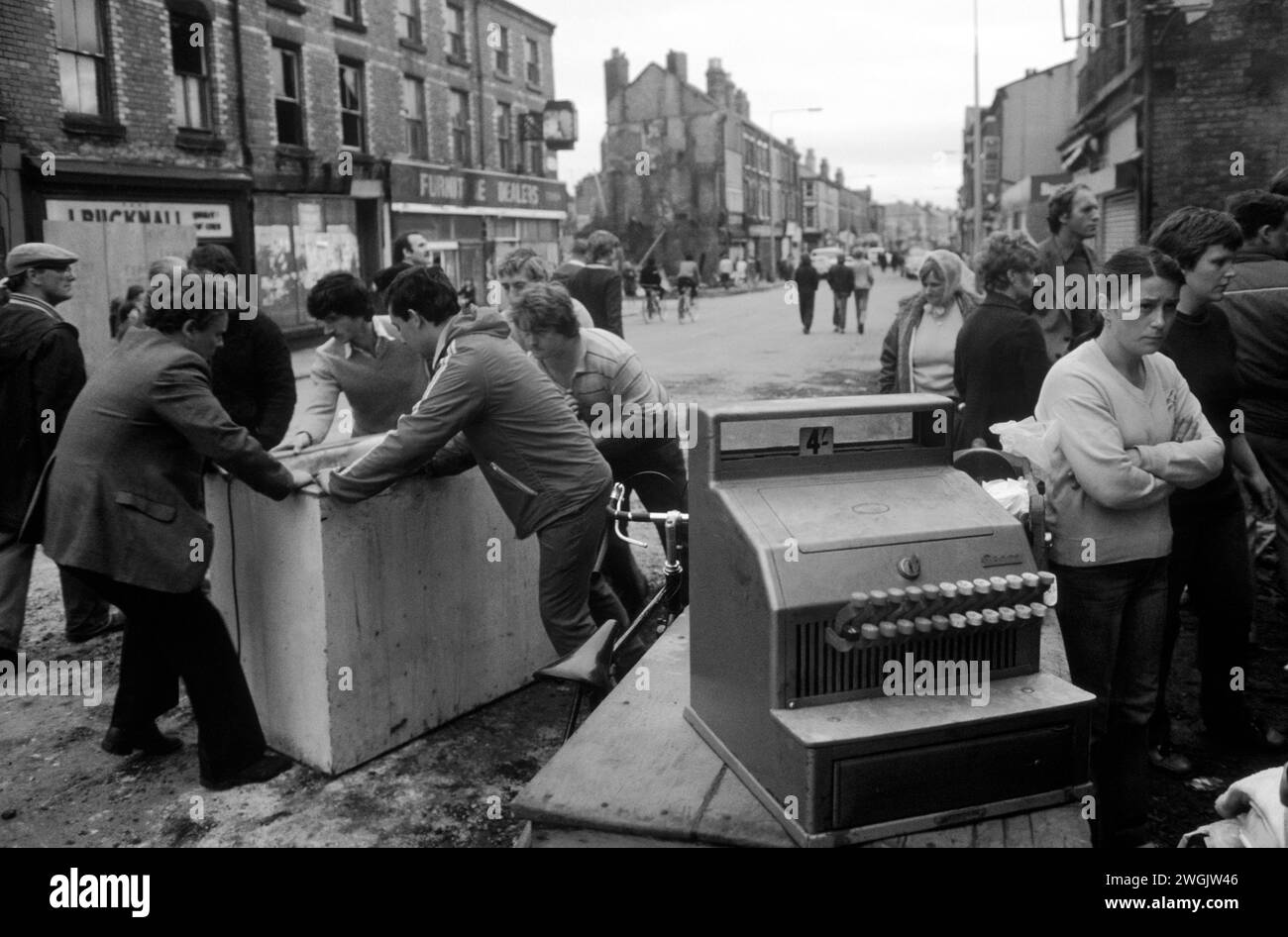 Toxteth Riots, Liverpool, England, Juli 1981. Am Morgen nach der Nacht der Unruhen, die einheimischen Männer, die sich mit dem Inhalt eines Burn-Out-Geschäfts begnügen. Sie plündern. Ein Ladenbesitzer, der mit dem 4 Schilling Schild aufhört, sind die Bewohner aufgeregt über das, was mit ihrer Nachbarschaft passiert ist. 1980S UK> HOMER SYKES Stockfoto