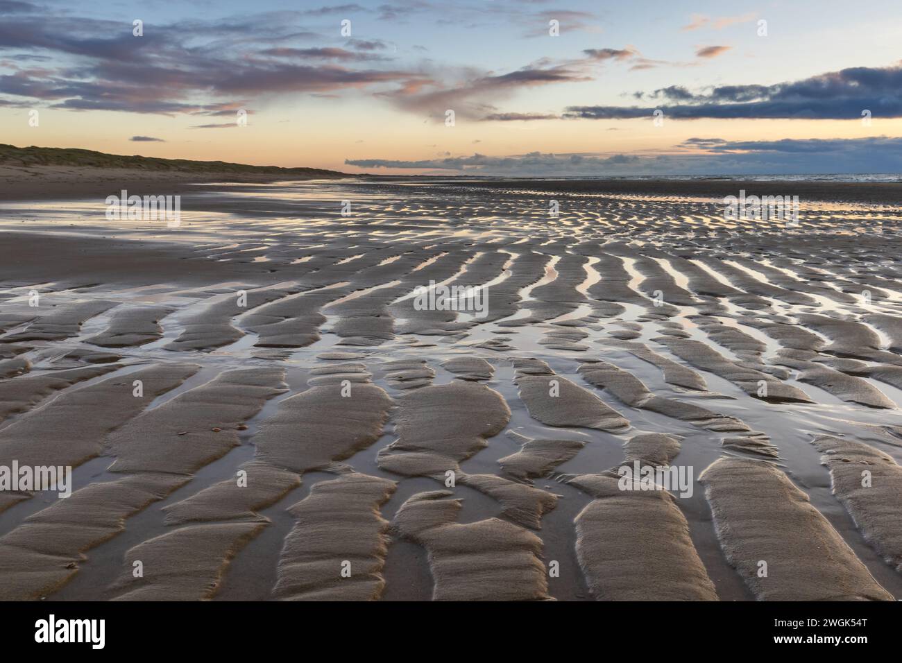 Das zurückziehende Meer lässt am Strand Wellen, beleuchtet von der untergehenden Sonne. Sobald sich das Meer zurückgezogen hat, bleiben an der Küste feste Sandkämme erhalten Stockfoto