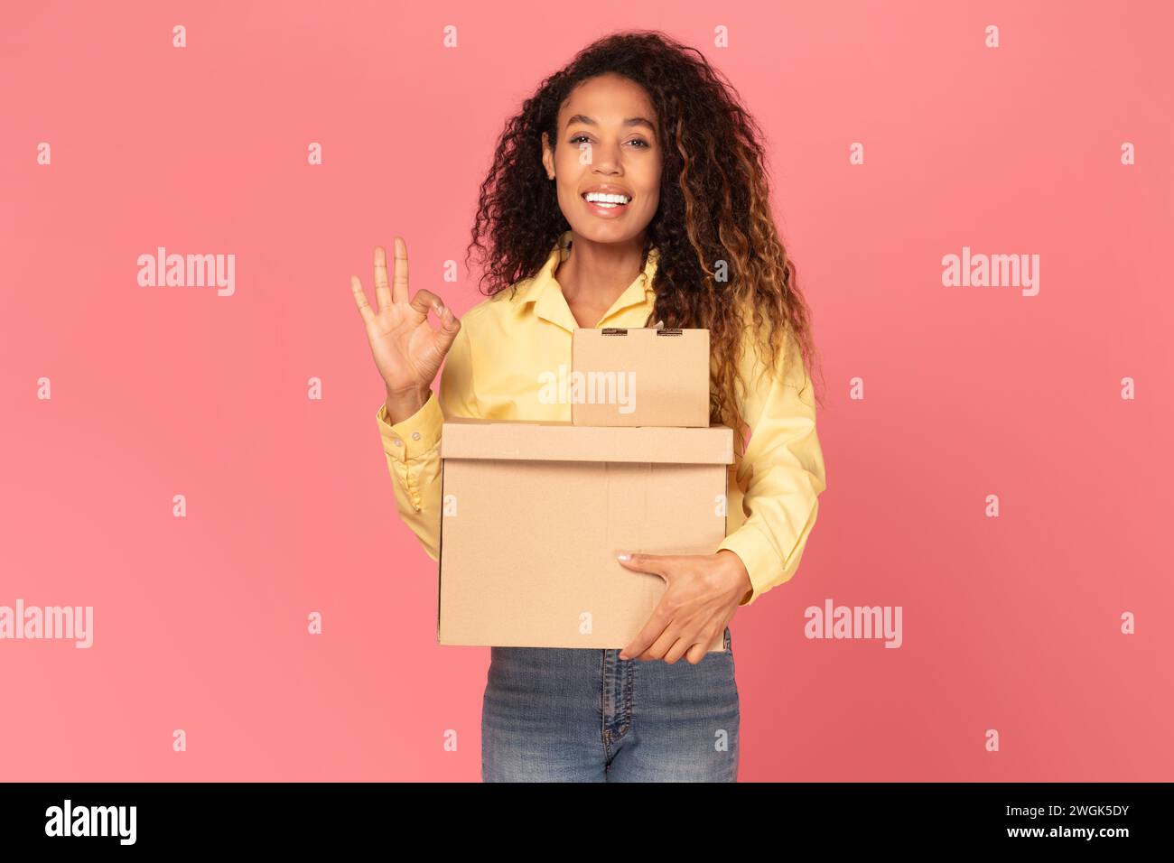 Eine junge schwarze Frau, die ein Paket hält und auf rosafarbenem Hintergrund gestickt hat Stockfoto