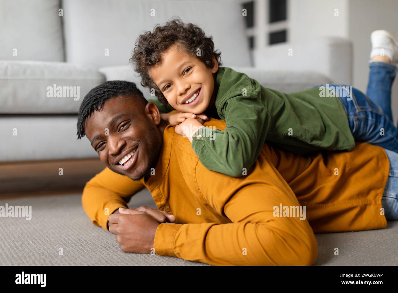 Schwarzer Vater und Sohn teilen sich einen spielerischen Moment auf dem Boden Stockfoto