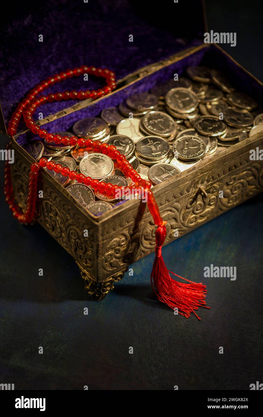 Eine Schatzkiste gefüllt mit VAE-Dirham-Münzen mit islamischem Rosenkranz. "Sharia-konforme Finanzen" - Ein konzeptionelles Bild. Stockfoto