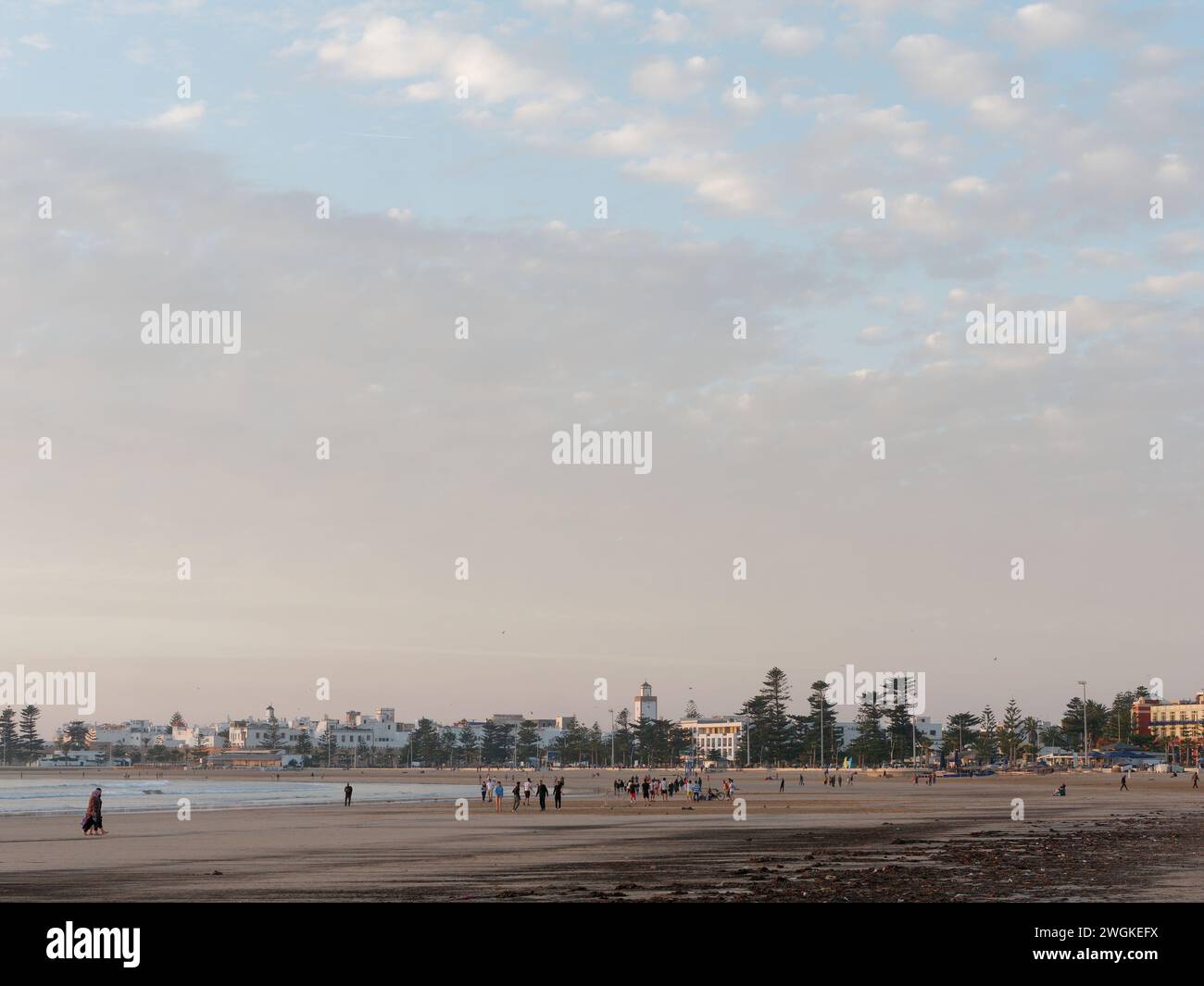 Menschen an einem Sandstrand, der sich dem Sonnenuntergang nähert, mit der historischen Medina dahinter in Essaouira, Marokko, 5. Februar 2024 Stockfoto