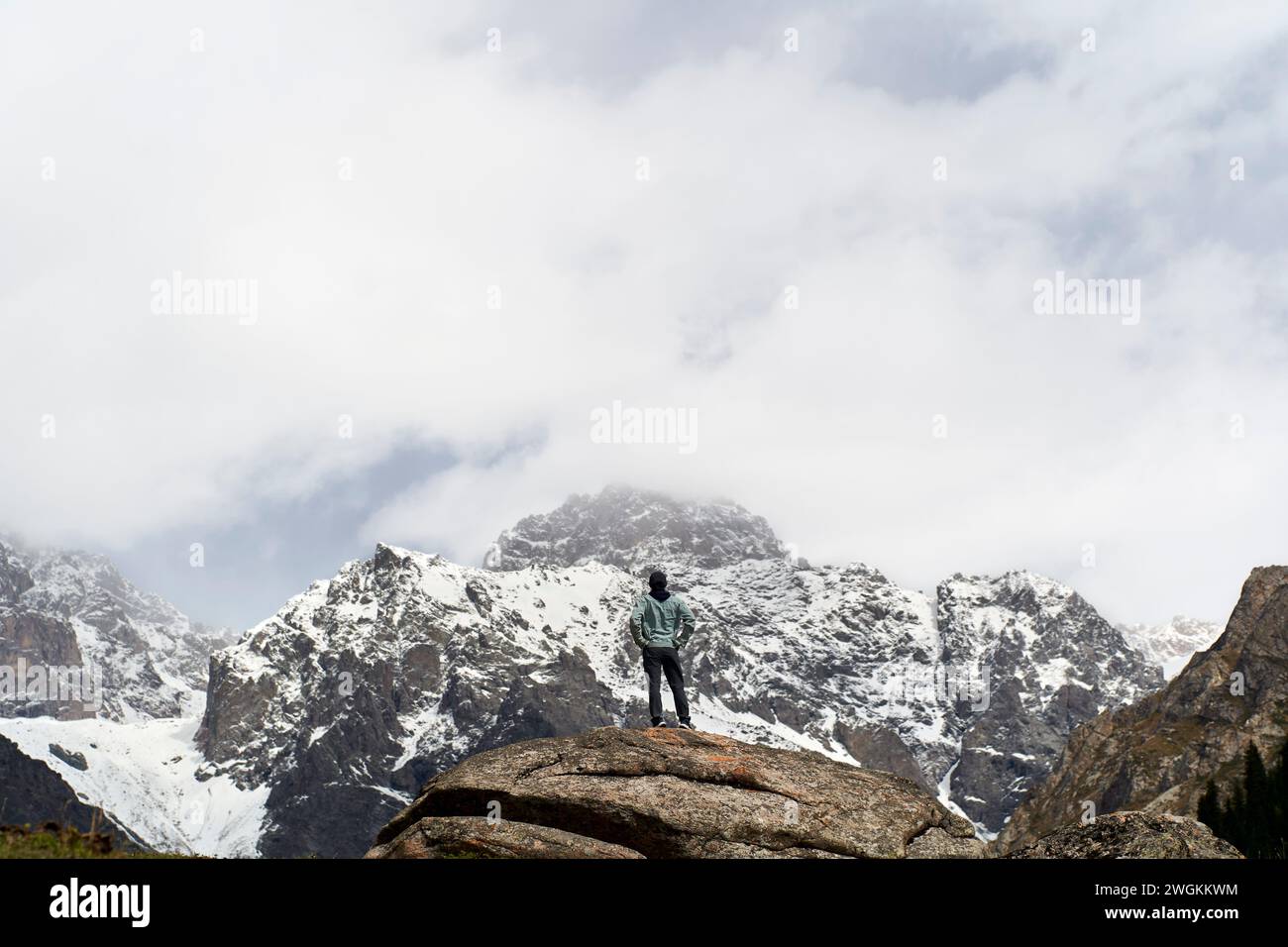 Rückansicht eines männlichen Reisenden aus asien, der auf einem Felsen steht und auf einen Schneeberg in Xinjiang, China, blickt Stockfoto