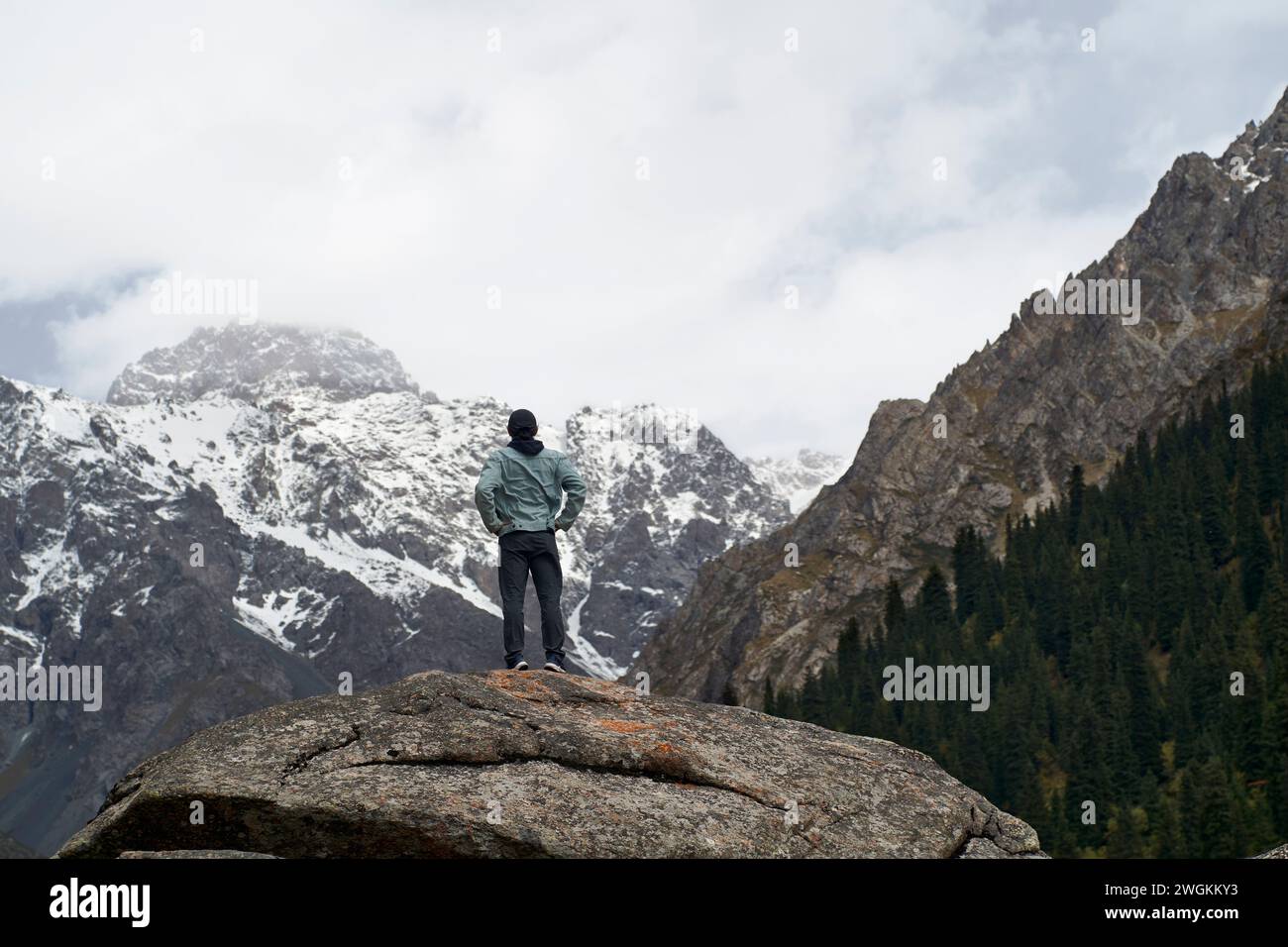 Rückansicht eines männlichen Reisenden aus asien, der auf einem Felsen steht und auf einen Schneeberg in Xinjiang, China, blickt Stockfoto