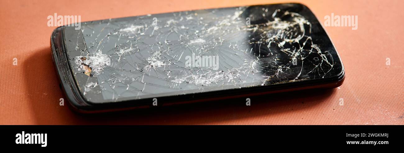 Smartphone mit kaputtem Bildschirm auf dem Tisch in der Werkstatt, Gerätereparatur, horizontales Banner Stockfoto