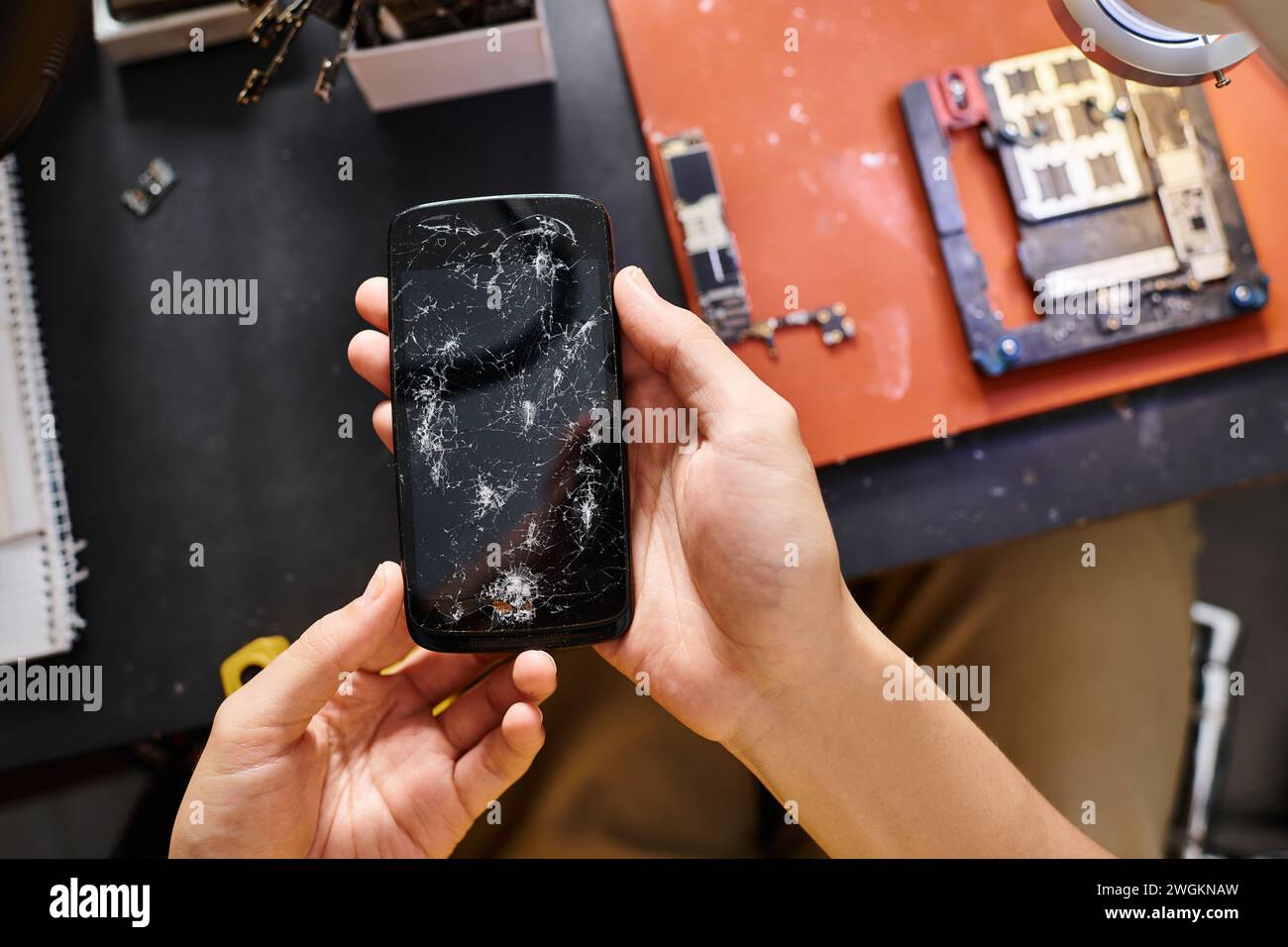 Mobiltelefon mit kaputtem Bildschirm in den Händen eines erfahrenen Technikers in der Reparaturwerkstatt, Kleinunternehmen Stockfoto