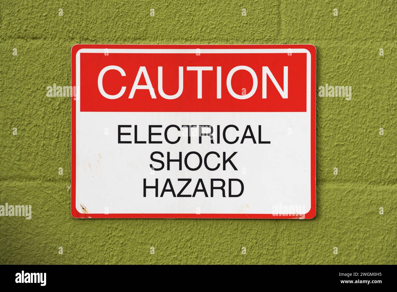 Rot-weißes und schwarzes Warnschild zur Warnung gegen Stromschlag an einer grünen Blockwand Stockfoto