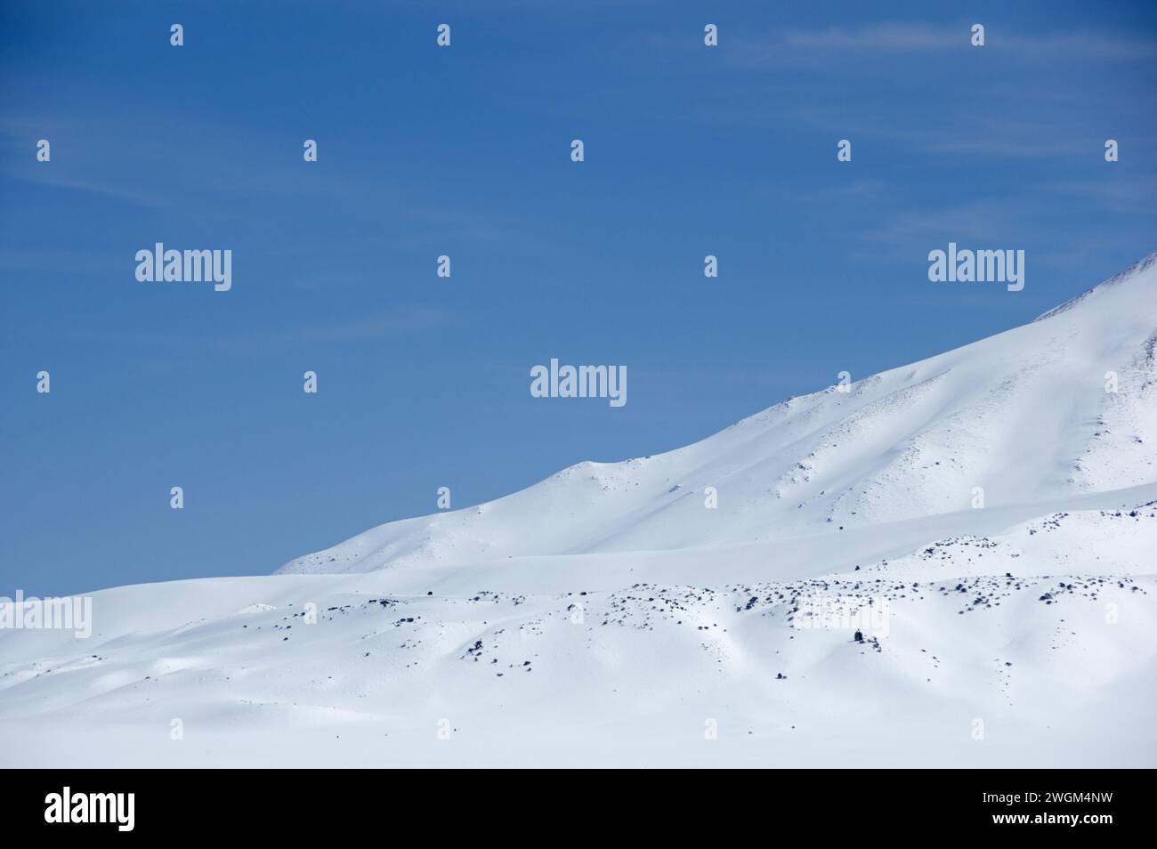 Winterlandschaft mit schneebedeckten Berghängen mit dunklen Felsen und Büschen und blauem Himmel Stockfoto