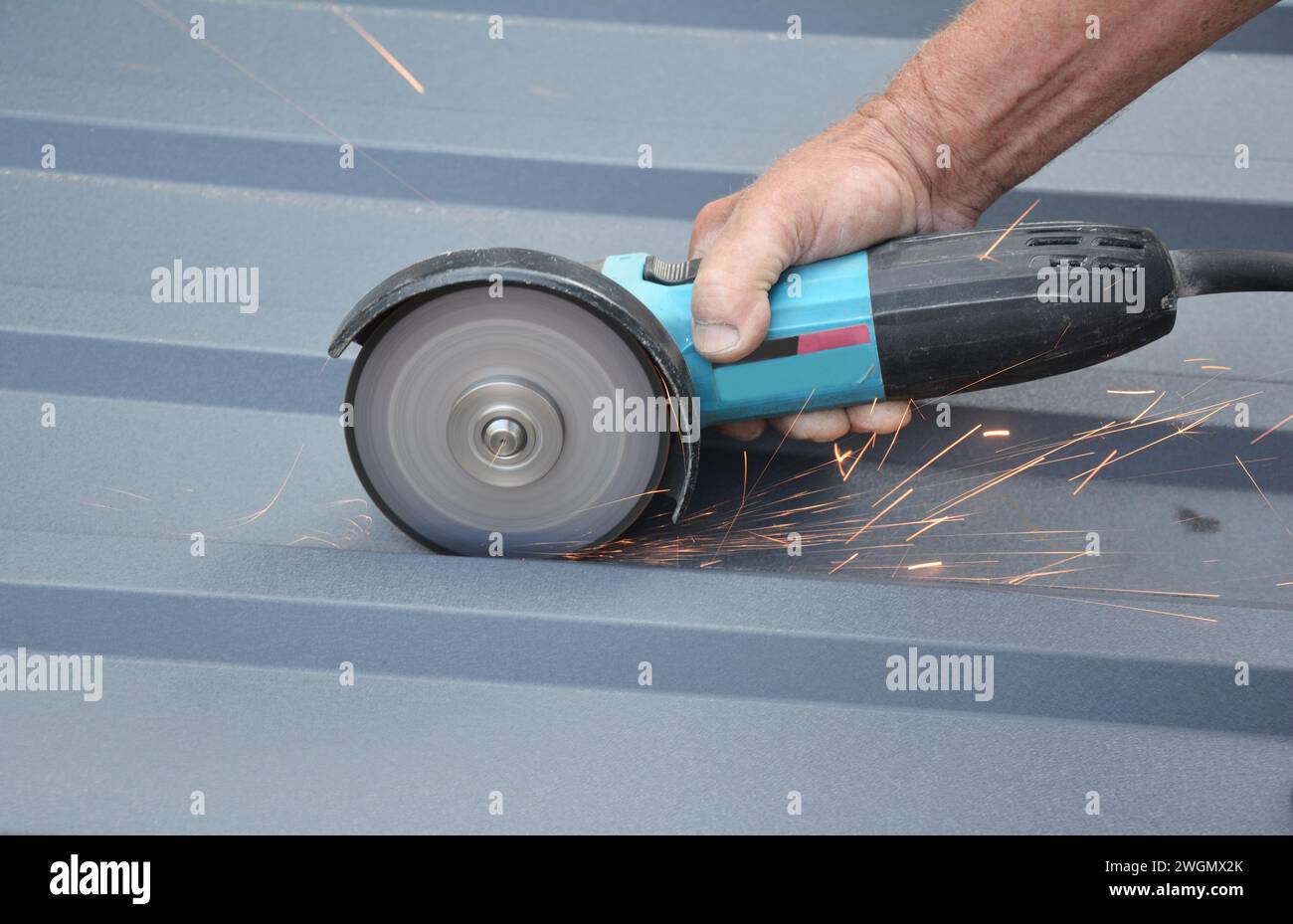 Dachkonstruktor schneidet mit einem Winkelschleifer ein Wellblech aus Metall. Schneiden von Dachziegeln aus Metall. Stockfoto