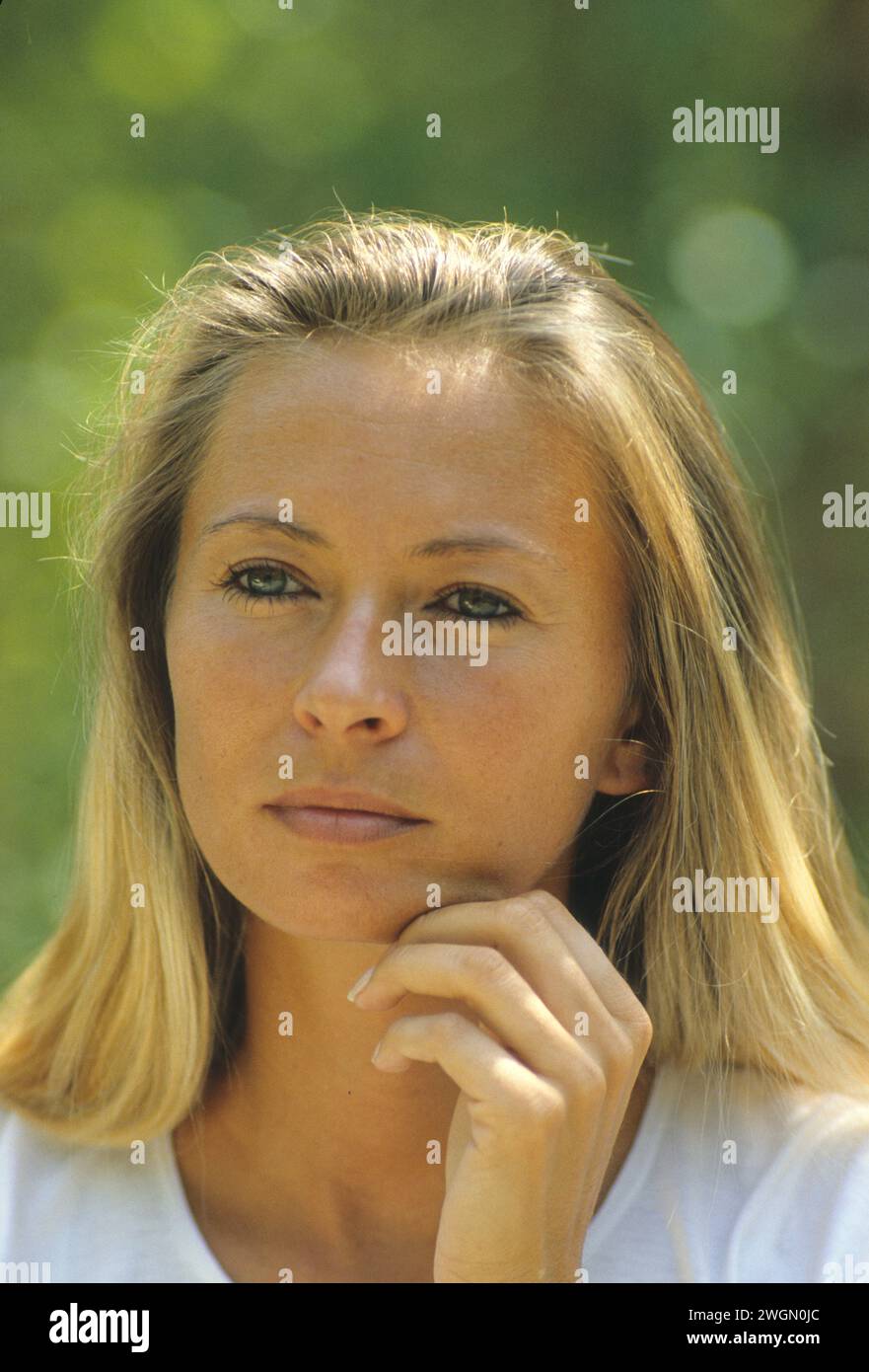 Hübsches blondes Haar junge Frau glückliches Denken natürliches gut aussehendes grünes Laub Hintergrund aussehende Frontkamera Stockfoto