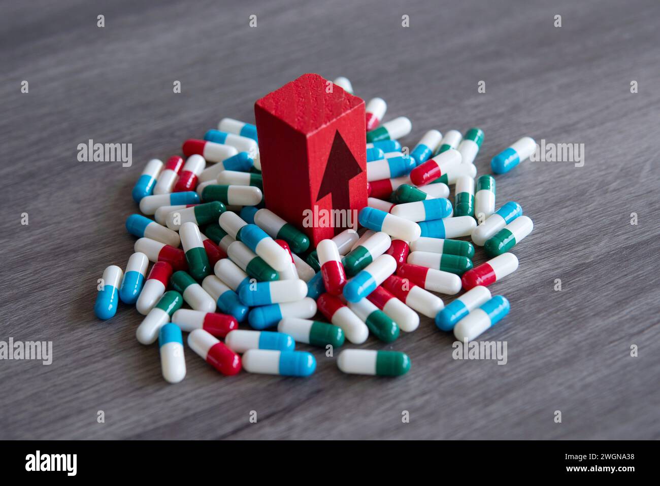 Ein roter Holzblock mit nach oben zeigendem Pfeil auf einem Haufen bunter Pillen. Steigende Kosten des verschreibungspflichtigen Medikamentenkonzepts. Stockfoto