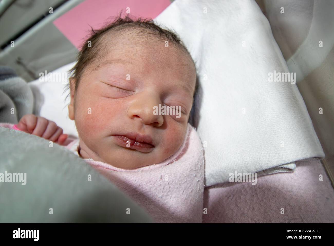 An ihrem ersten Lebenstag trägt ein neugeborenes Mädchen ein rosafarbenes Krankenhaus-ID-Armband an ihrer Hand Stockfoto