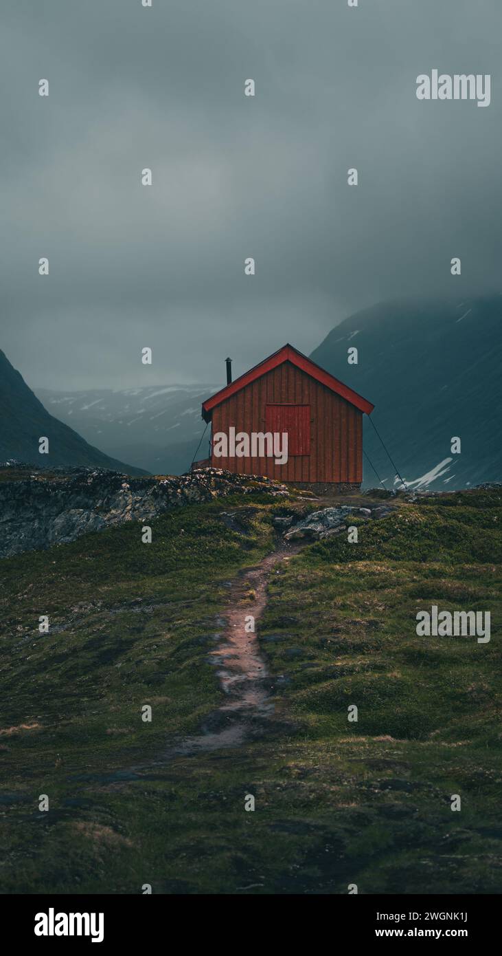 Ein altes rotes Haus auf einem norwegischen Berg mit einem malerischen Pfad und einer Kulisse. Stockfoto