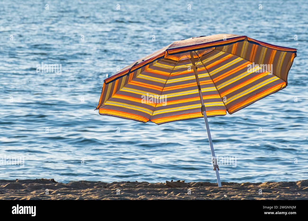 Gestreifter Sonnenschirm in der Nähe von Handtüchern am Strand. Sonnenschirm an einem sonnigen Tag. Sonnenschirm. Niemand, Kopierraum für Text, Reisefoto Stockfoto