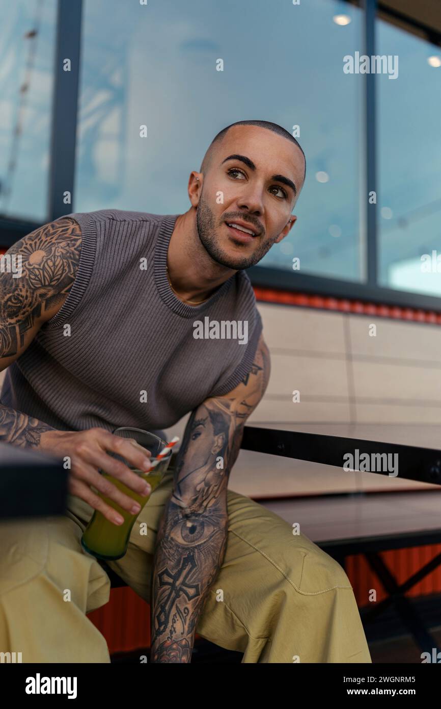 Ein hübscher junger Mann mit Tattoos, der ein Glas Limonade vor einem Restaurant hält Stockfoto