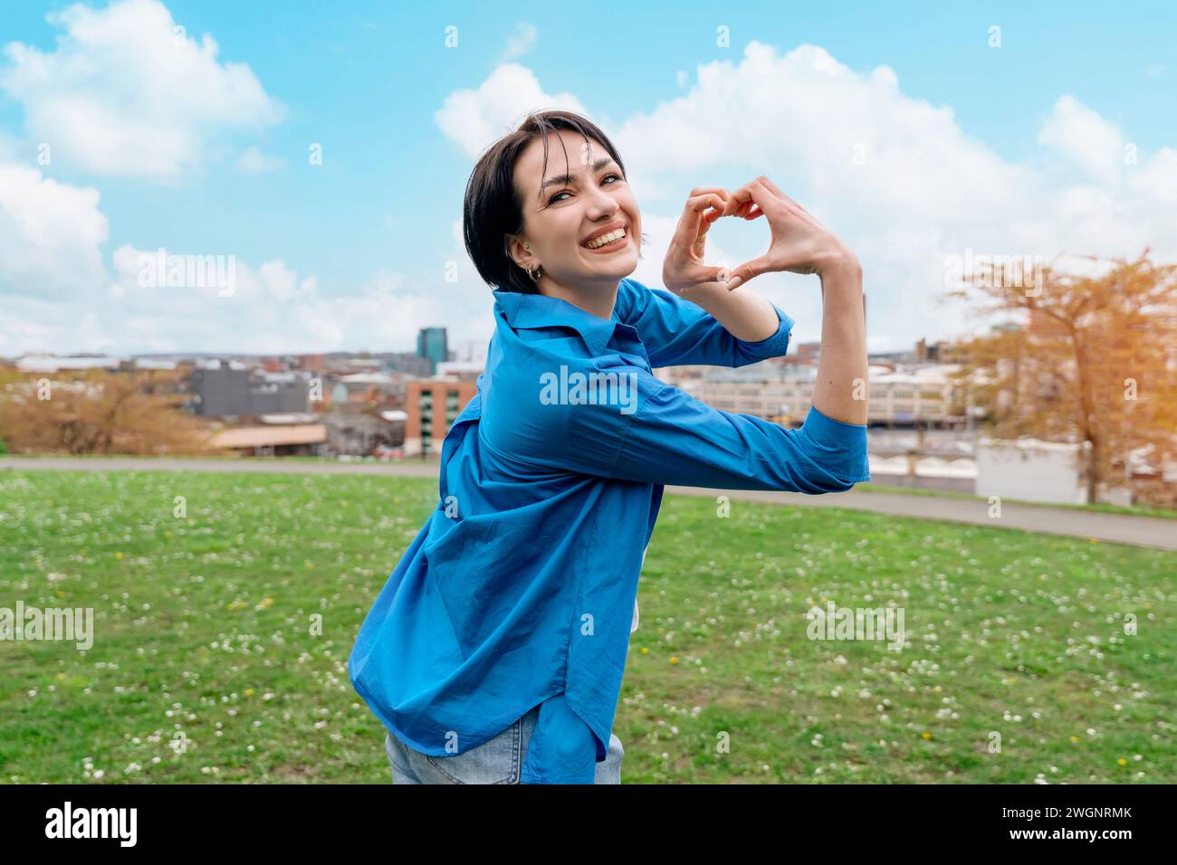 Eine junge Frau mit herzförmigen Händen im Park ‌ Sommertag Fall in Love Konzept Stockfoto