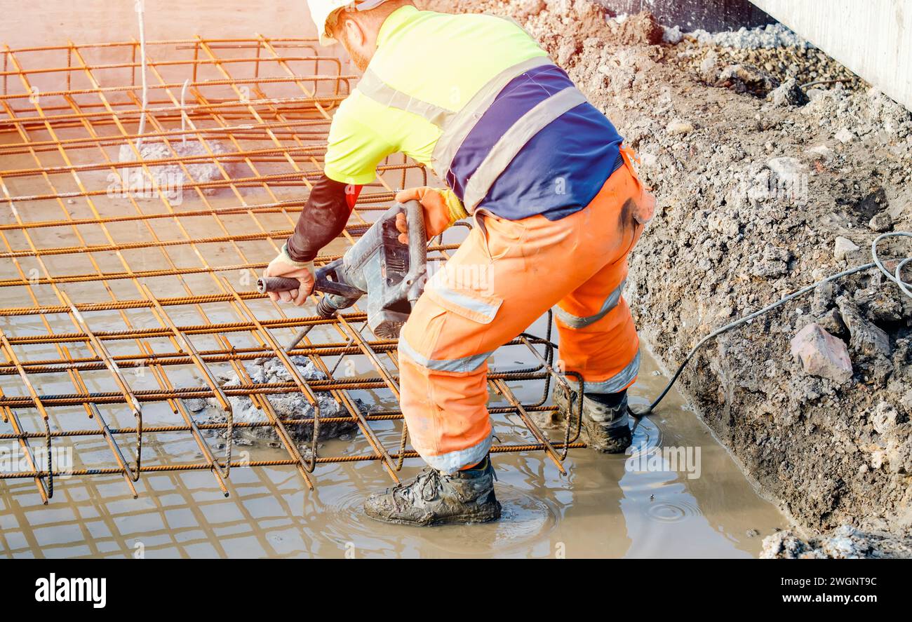 Der Baumeister verwendet einen elektrischen Bremser, um Beton von der Oberseite des Stapels zu brechen, um den Bewehrungskäfig darauf zu montieren Stockfoto