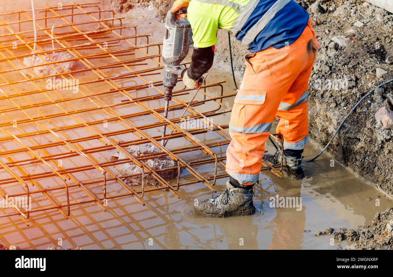 Der Baumeister verwendet einen elektrischen Bremser, um Beton von der Oberseite des Stapels zu brechen, um den Bewehrungskäfig darauf zu montieren Stockfoto