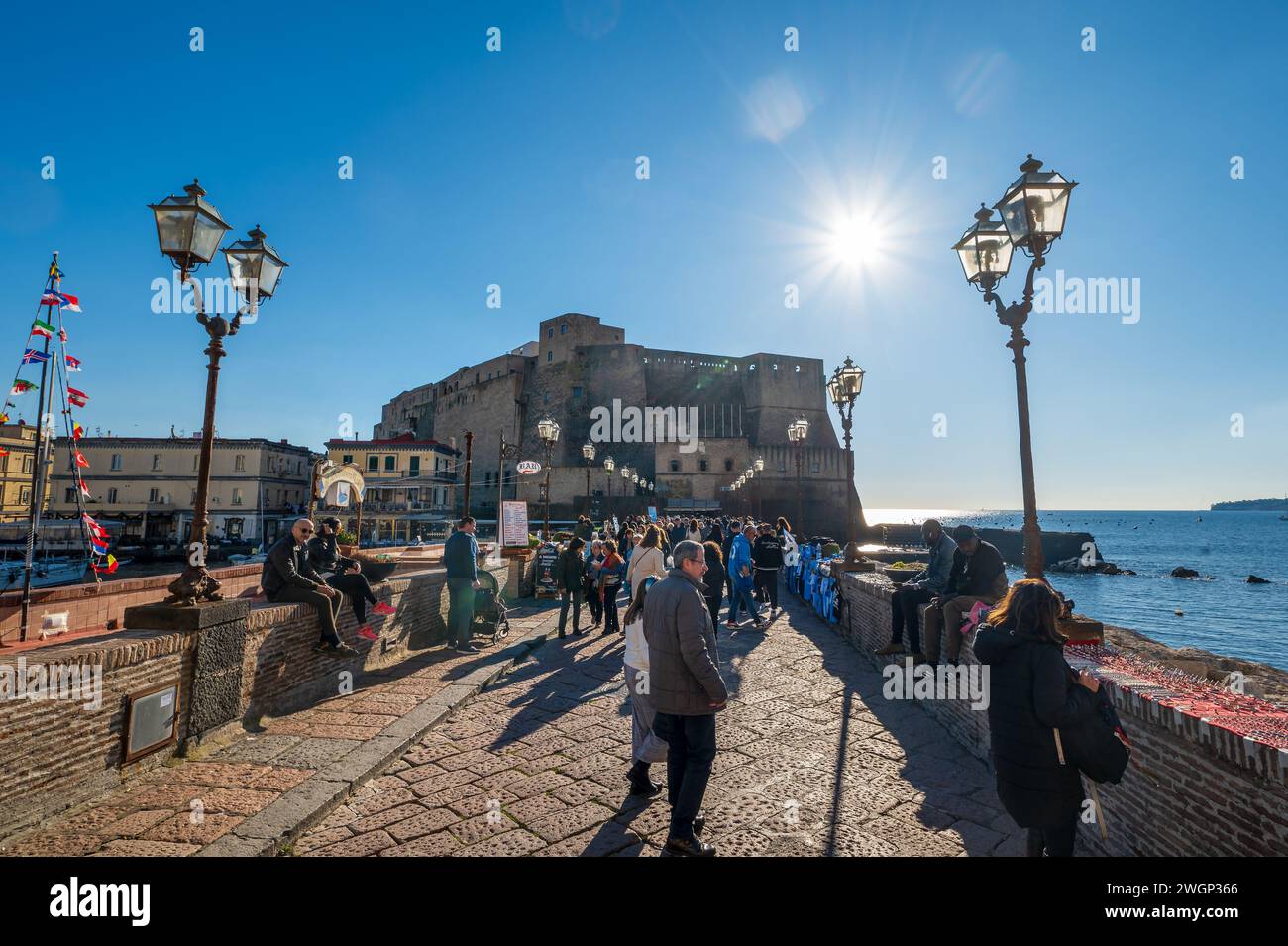 Neapel, Italien - 18. Dezember 2022: Überfüllte Brücke, die zum majestätischen Stein der Burg Ovo führt, steht stolz auf einer felsigen Insel. Das berühmte Castel dell'Ovo ist ein Juwel Stockfoto