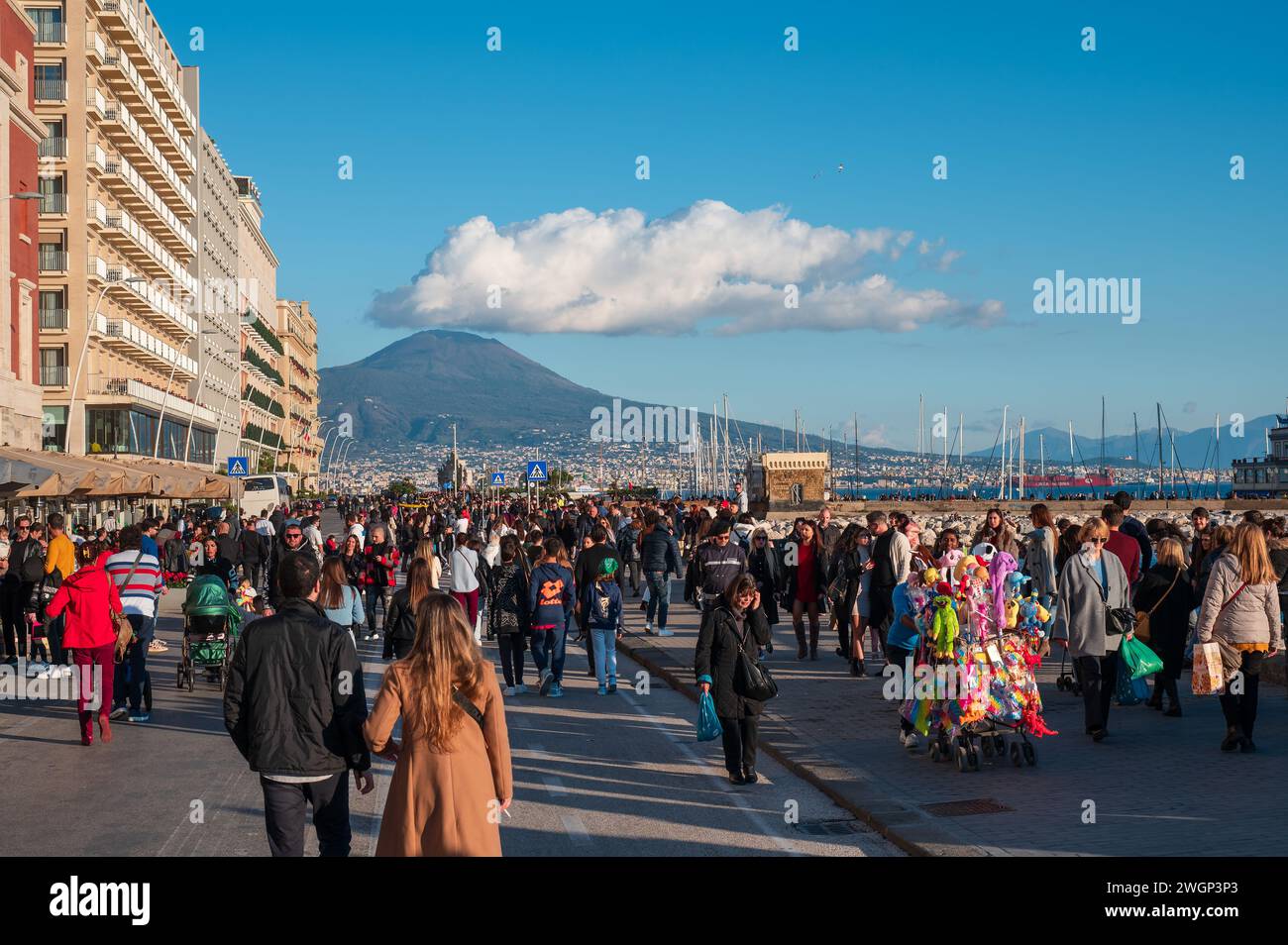Neapel, Italien - 18. Dezember 2022: Eine geschäftige Menge von Touristen und Einwohnern, die vor einer majestätischen Kulisse des Vesuv-Vulkans spazieren Stockfoto