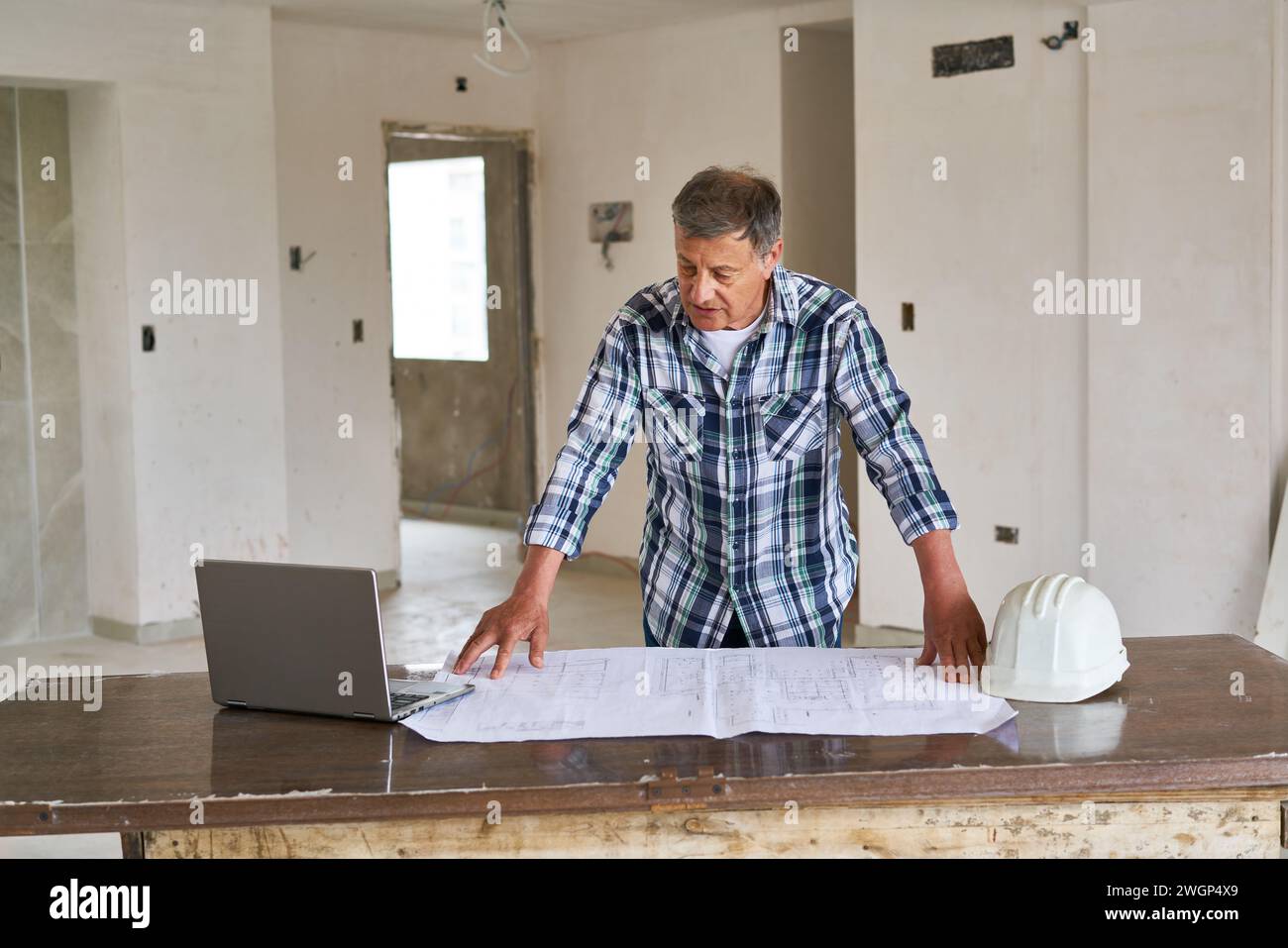 Leitender Architekt, der den Plan am Schreibtisch im Haus analysiert Stockfoto