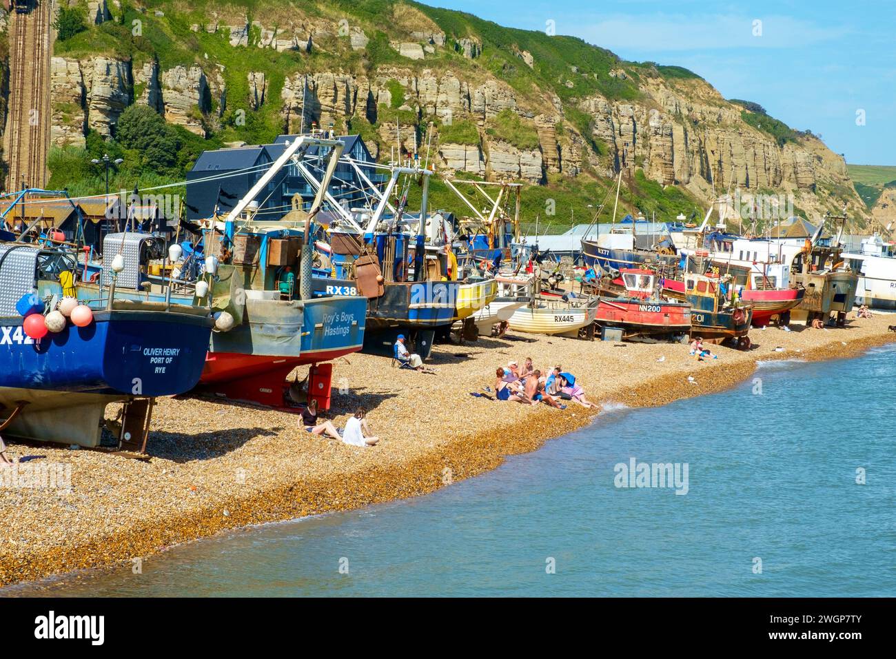 Menschen, die sich am Strand von Hastings Fishing Boat Beach in Est Sussex, Großbritannien, sonnen Stockfoto