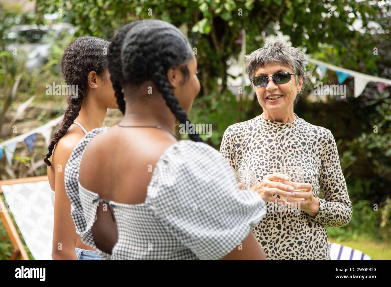 Eine reife weiße Frau plaudert und lacht mit zwei jungen schwarzen Frauen auf einer Gartenparty Stockfoto