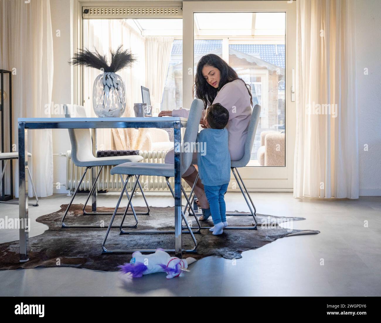 Schöne asiatische Frau, die von zu Hause an ihrem Küchentisch arbeitet. Während sie sich um ihren Sohn kümmert Stockfoto