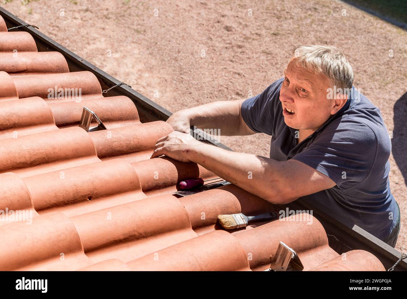 Ein reifer Mann überprüft die Dachziegel des Hauses. Stockfoto