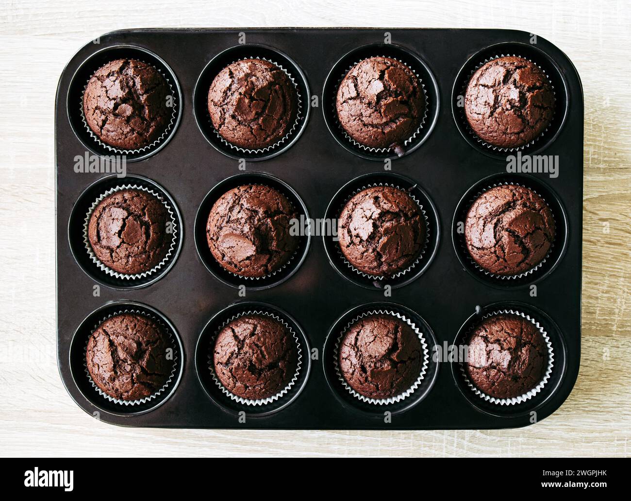 Über dem Blick auf kleine gebackene Schokoladenmuffins in der Muffinpfanne drinnen im Haus auf Holzhintergrund. Kreativer Hintergrund. Stockfoto