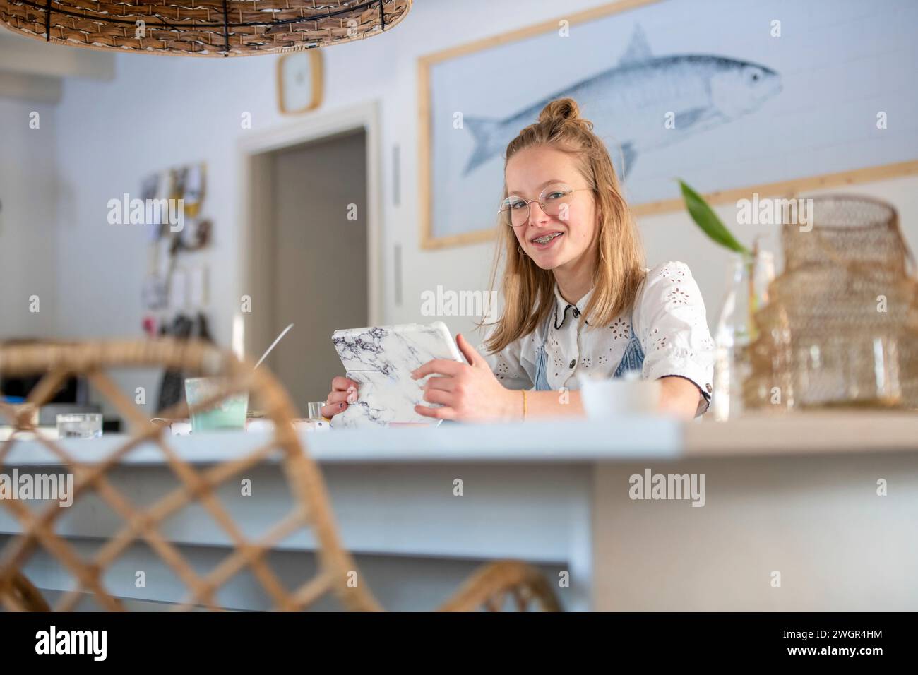 Porträt der blonden attraktiven jungen Frau auf ihrem Tablet am Küchentisch Stockfoto