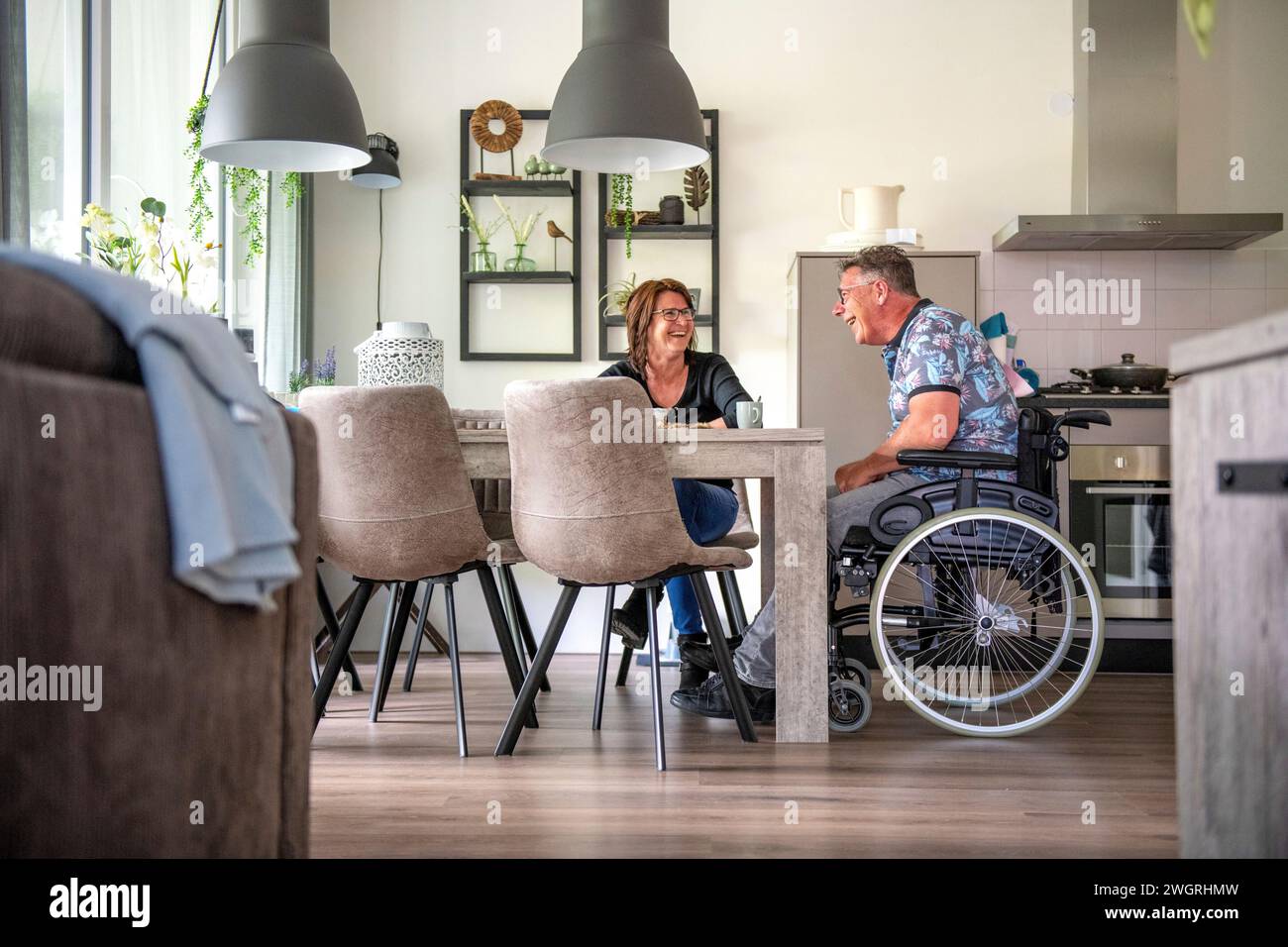 Die Frau bereitet ihr Mittagessen vor, der in seinem Rollstuhl am Tisch sitzt Stockfoto