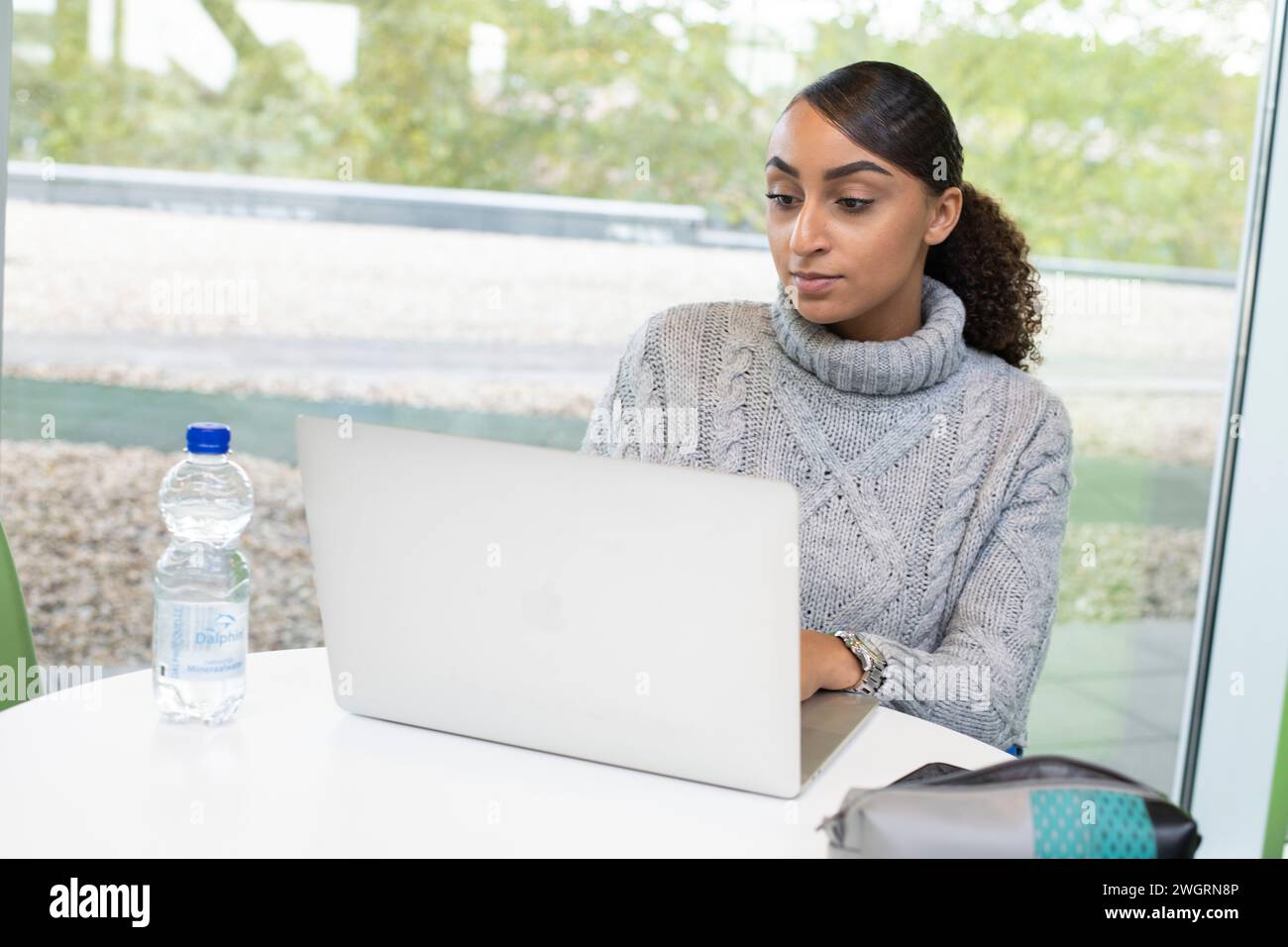 Weibliche professionelle gemischte Rasse arbeitet an ihrem Laptop an einem kleinen Schreibtisch im Gemeinschaftsbereich Stockfoto