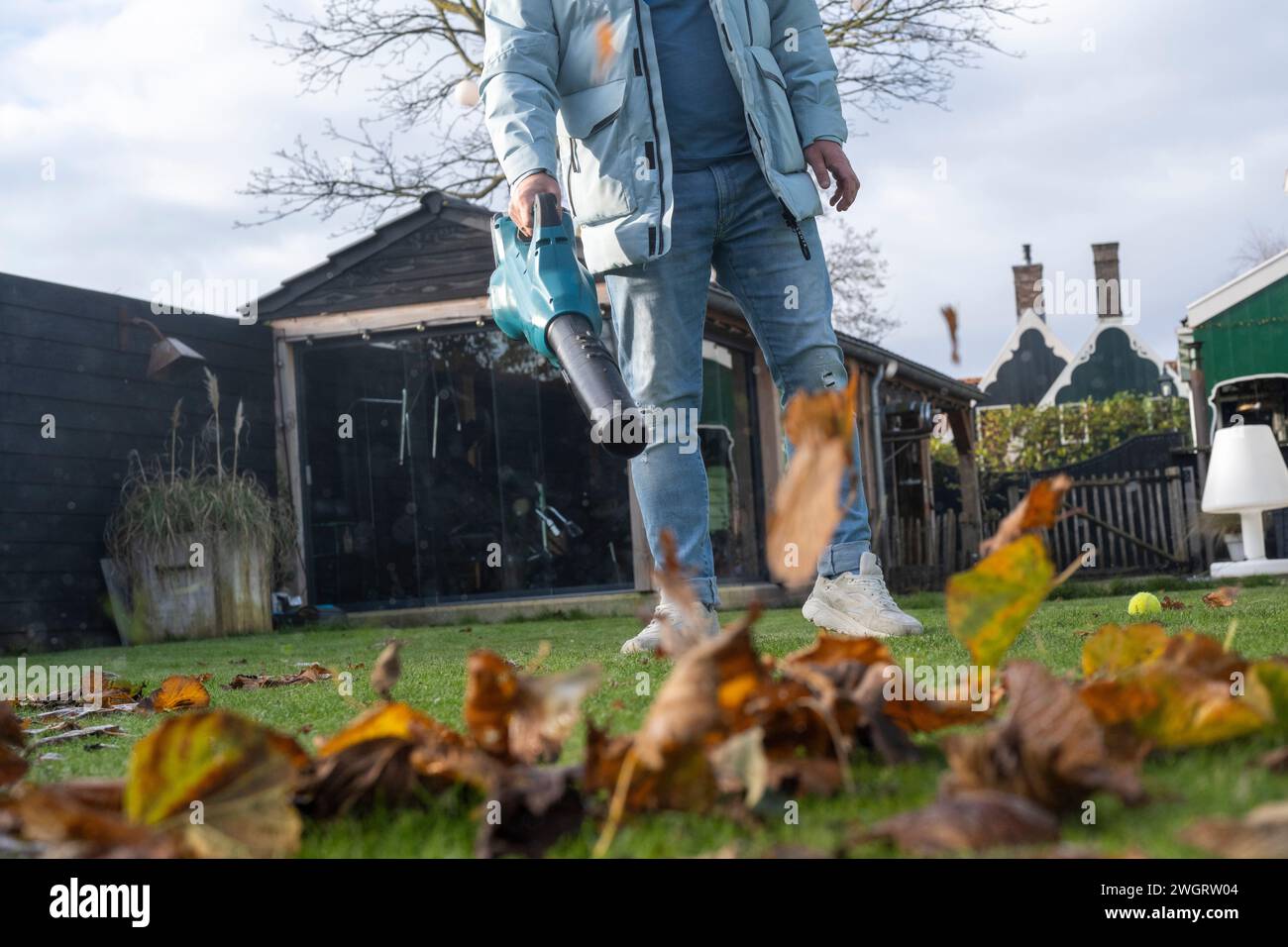 Mann, der ein elektrisches Gebläse benutzt, um Blätter im Garten seines Hauses aufzuräumen Stockfoto