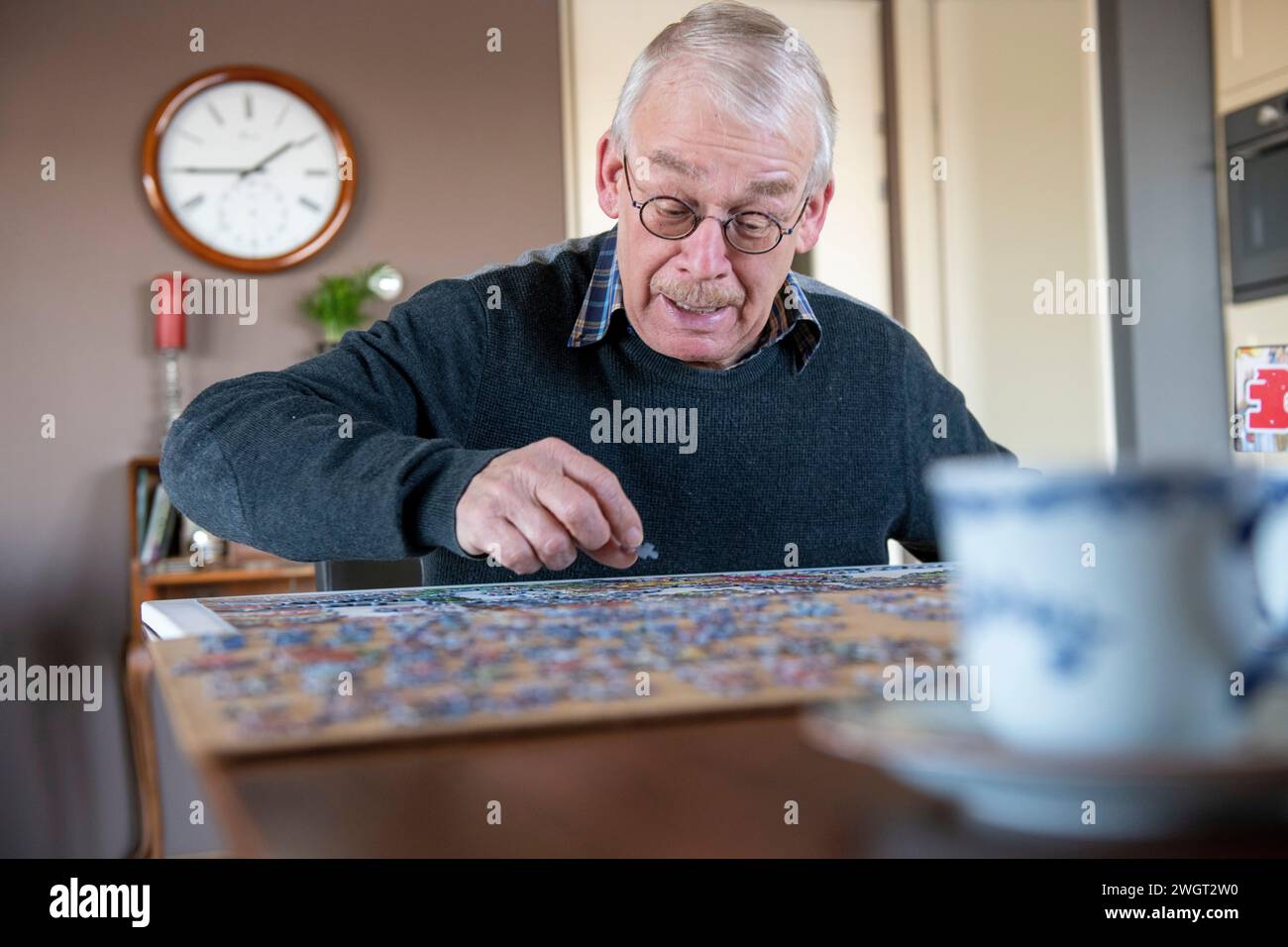 Ein pensionierter Mann, der mit einem Puzzle beschäftigt ist und an seinem Esstisch sitzt Stockfoto