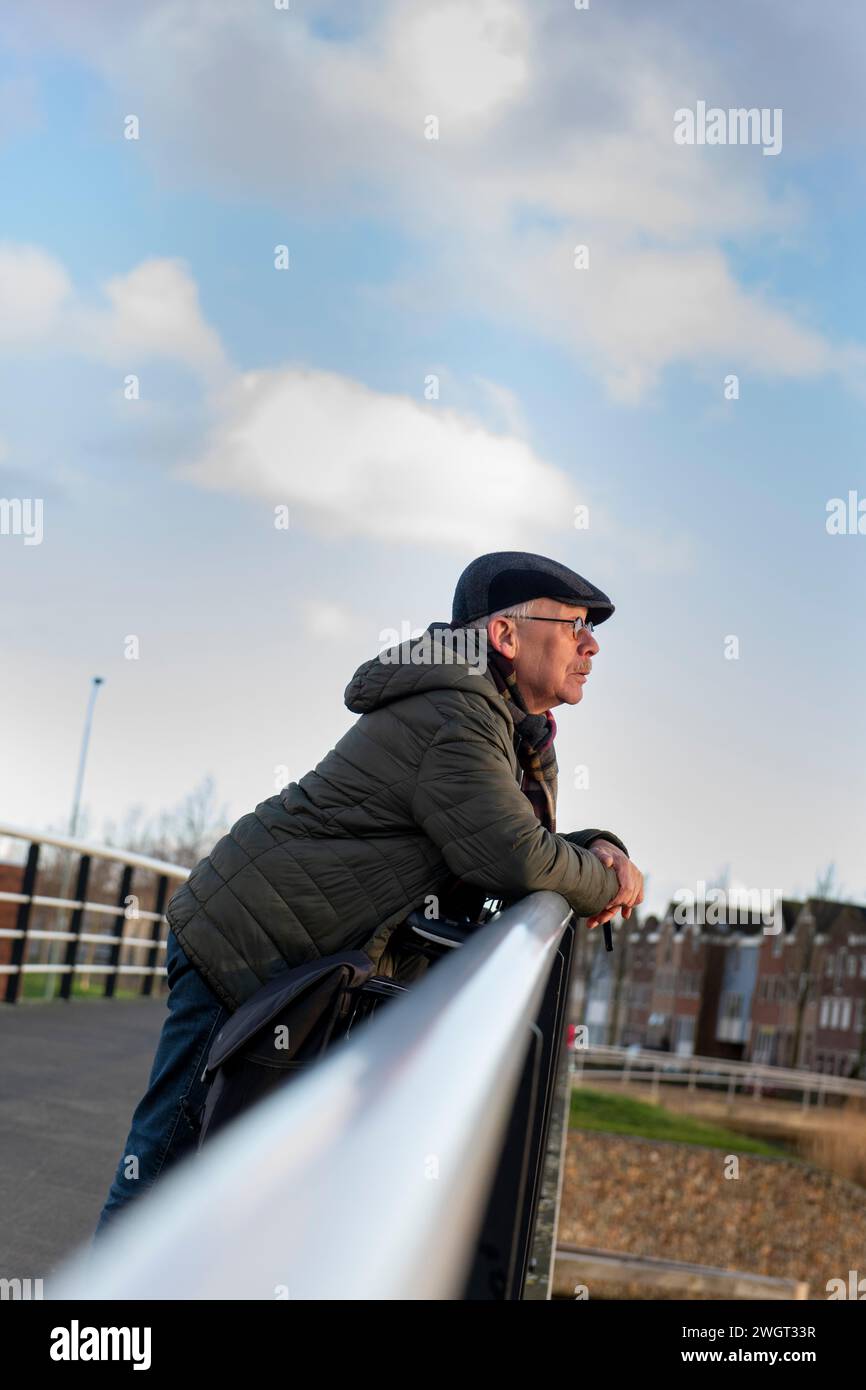 Ein älterer Mann geht gesund spazieren und lehnt sich auf ein Geländer und blickt auf die Landschaft Stockfoto