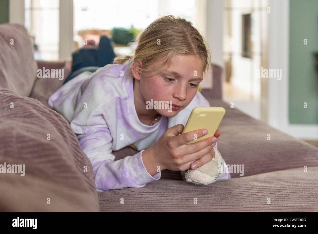 Junge Teenagerin, die sich auf dem Sofa entspannt und mit ihrem Telefon recherchiert Stockfoto