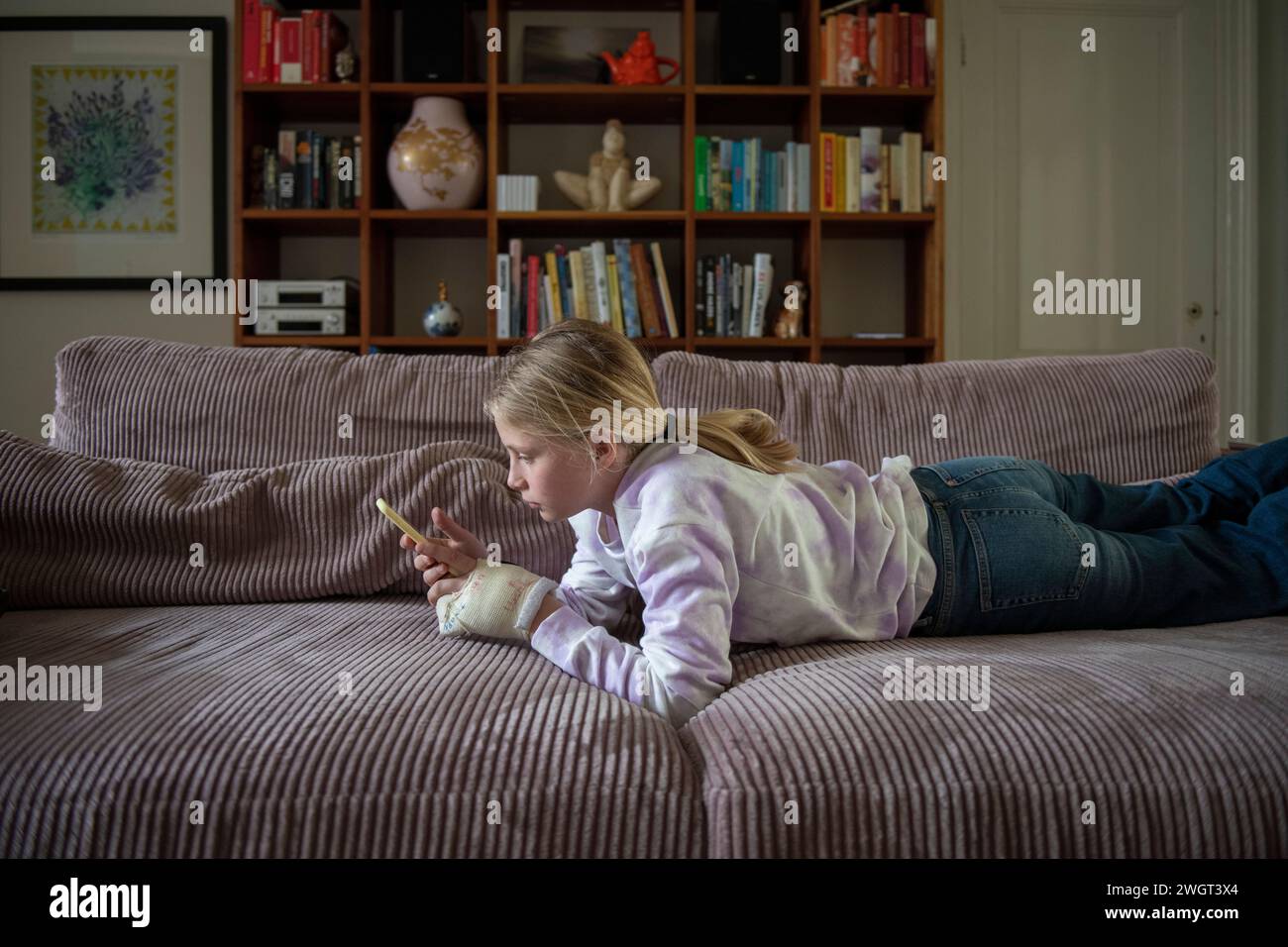 Junge Teenagerin, die sich auf dem Sofa entspannt und mit ihrem Telefon recherchiert Stockfoto